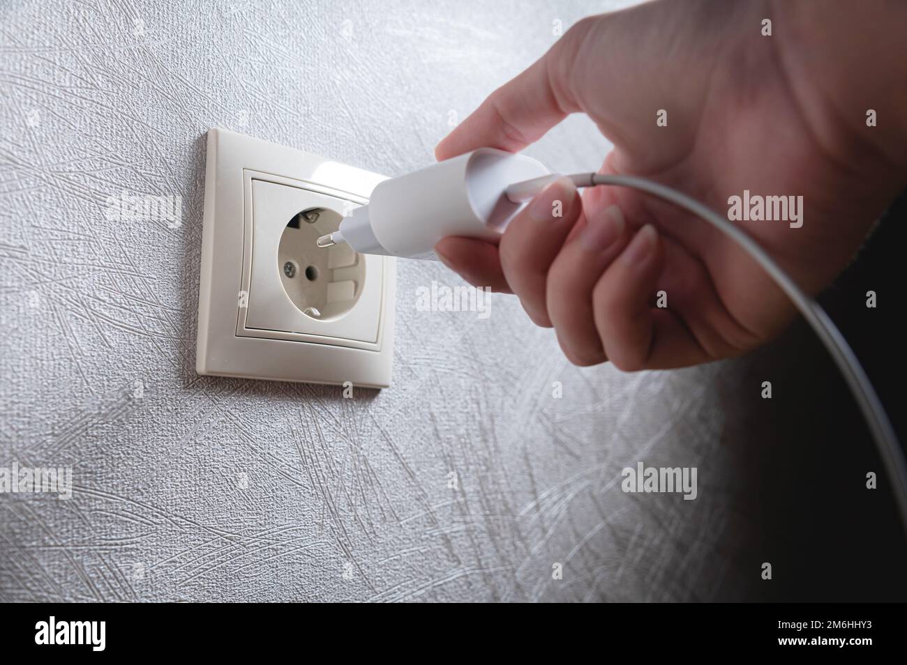 Nahaufnahme der Hand einer Frau, die ein weißes usb-Ladegerät in eine 220-Volt-Steckdose einsteckt Stockfoto