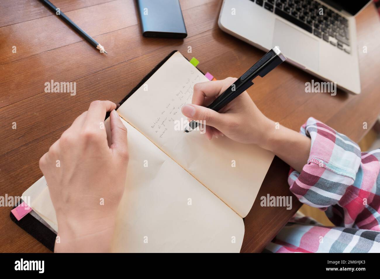 Junge kaukasische attraktive Frau, die Notizen in ihrem Notizbuch macht, während sie in der Küche am Tisch sitzt. Schreibpapier Notizbuch Stockfoto