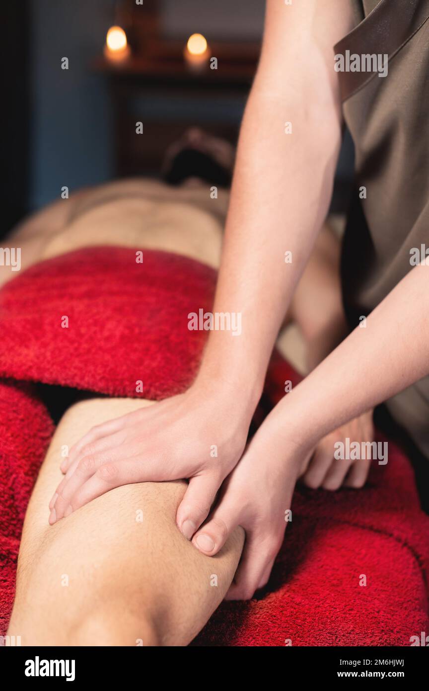 Professionelle männliche Sportmassage der Hüfte und des Knies in einem dunklen Massageraum. Premium-Massagen. Speicherplatz kopieren Stockfoto