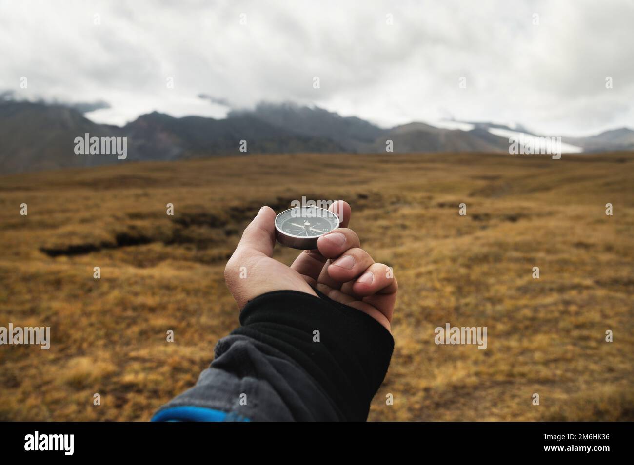Die Hand eines Reisenden hält einen magnetischen Kompass vor dem Hintergrund einer Berglandschaft und niedriger Wolken an einem sonnigen Tag Stockfoto