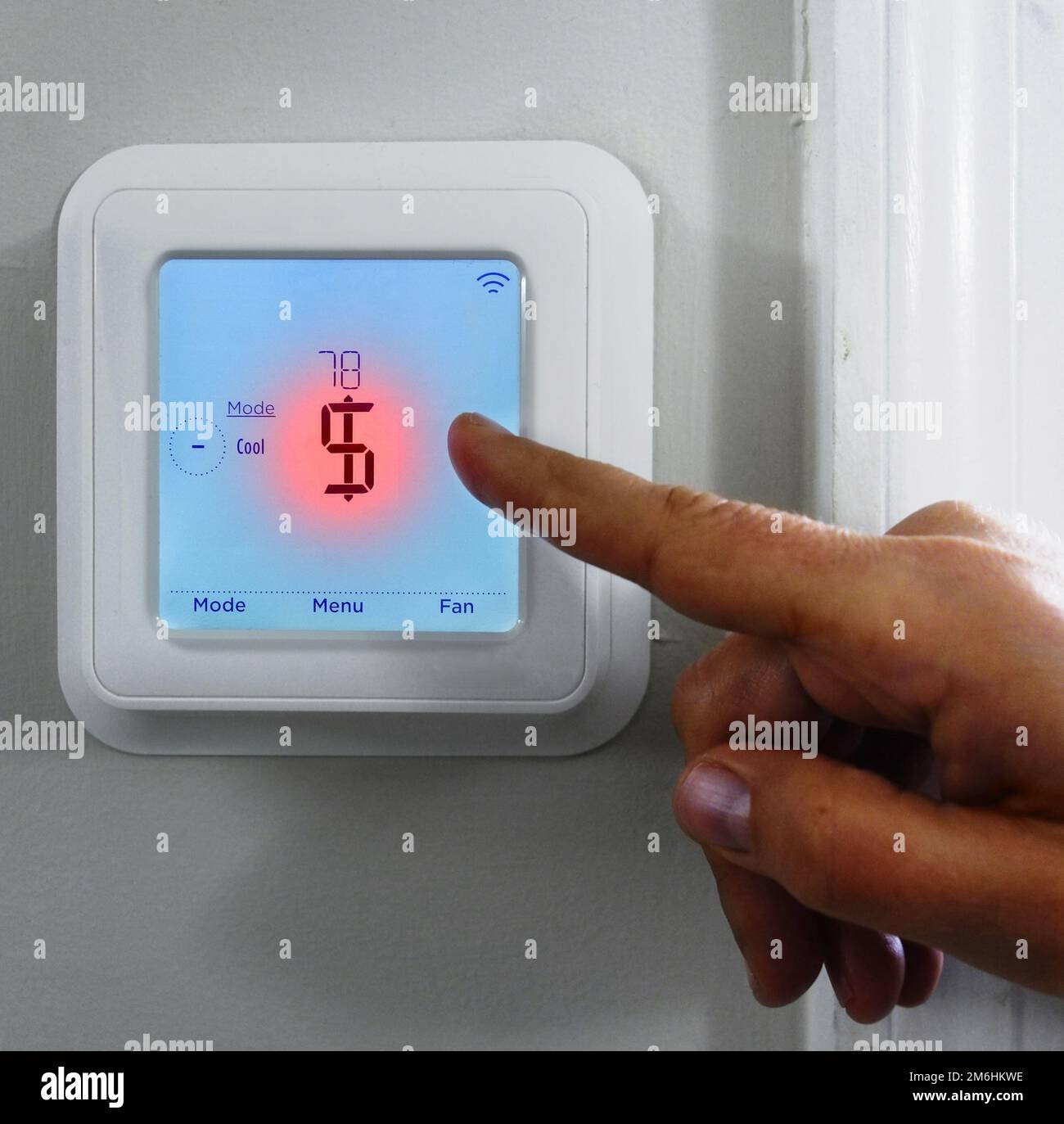 Zeige mit dem Finger auf ein rotes Dollarzeichen auf einem intelligenten Thermostat -- Kostenkonzept für Heizung und Kühlung Stockfoto