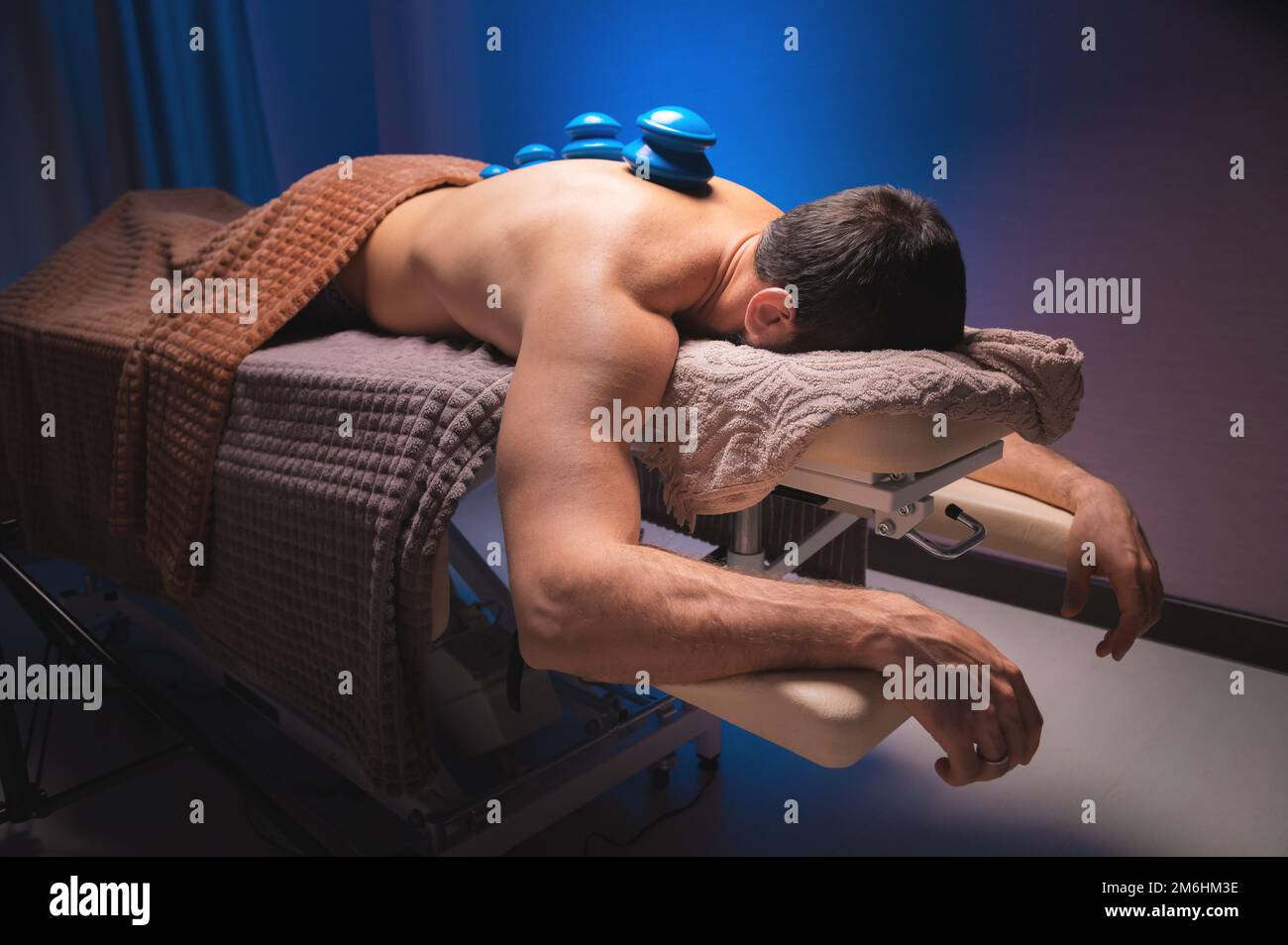 Mann, der sich hinlegt, erholt sich mit Vakuumbechern gesund. Nahaufnahme von Vakuumbechern auf der Rückseite eines Mannes vor einem schwarz-blauen Hintergrund. Stockfoto