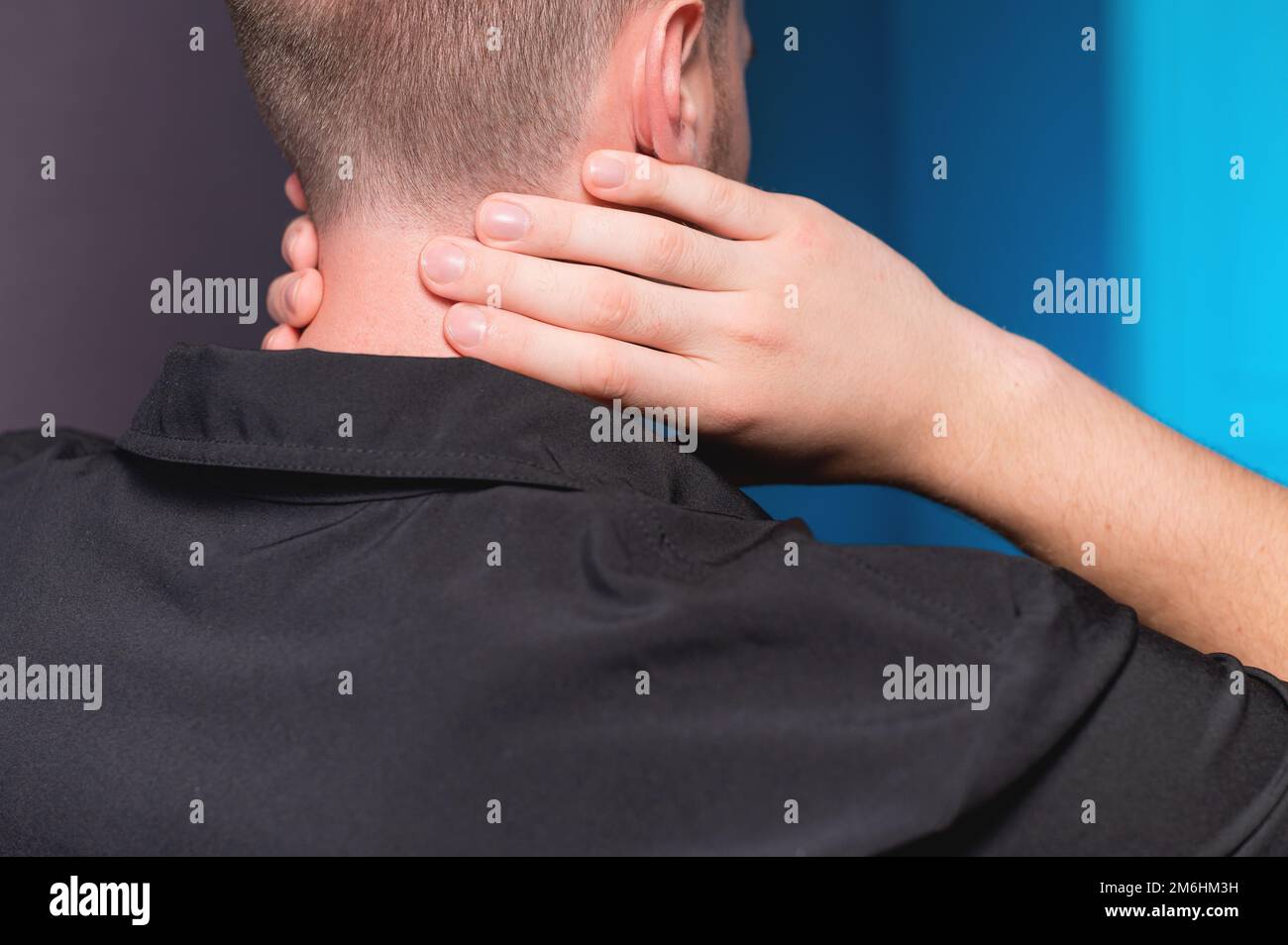 Nahaufnahme. Ein freiberuflicher Mann in einem dunklen Hemd hat nach langer Arbeit Halsschmerzen und massiert sich den Hals selbst. Stockfoto