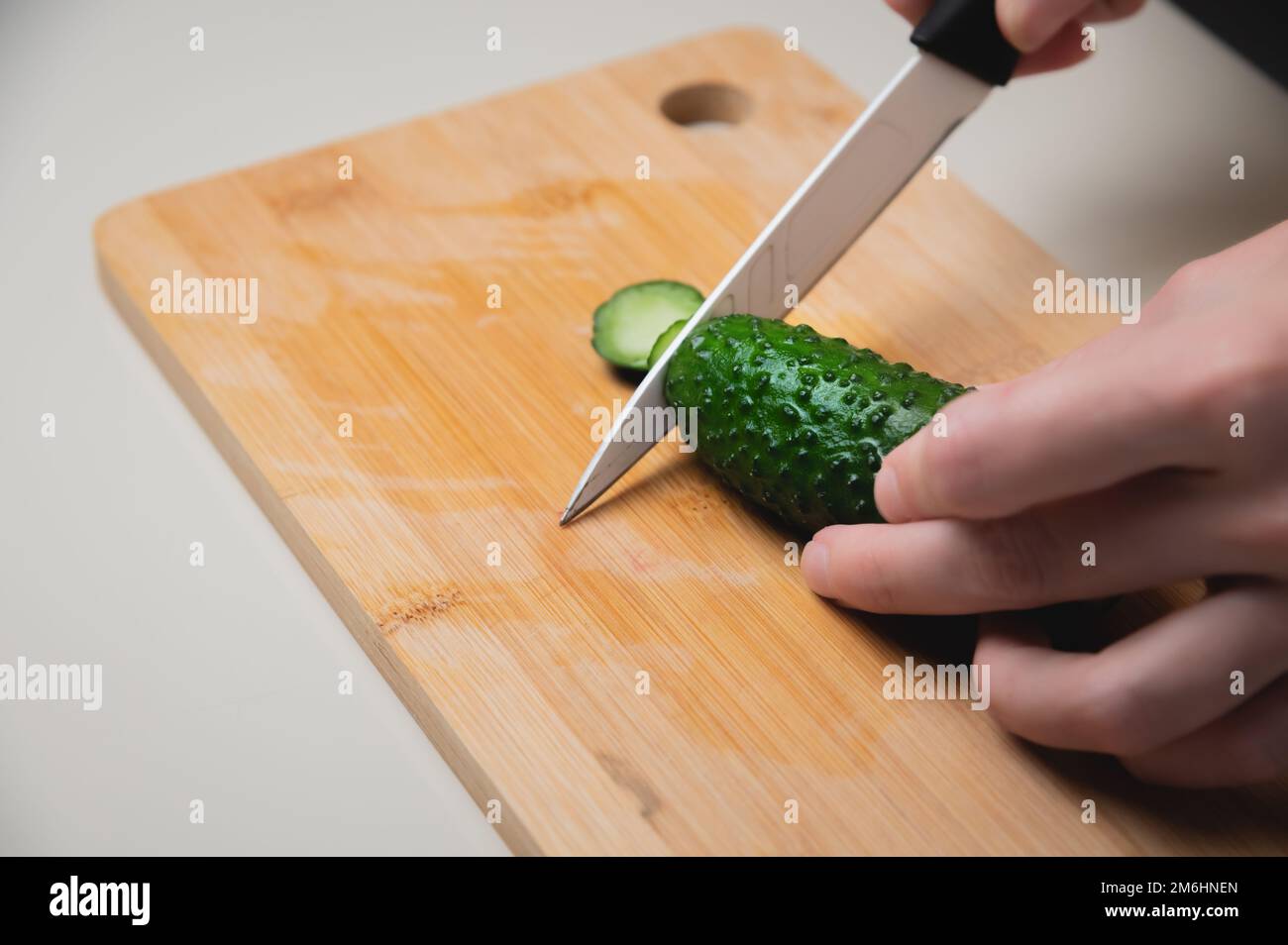 Nahaufnahme von weiblichen Händen, die Gurken für einen veganen Salat schneiden. Hausmannskost gesunde und gesunde Lebensmittel Stockfoto