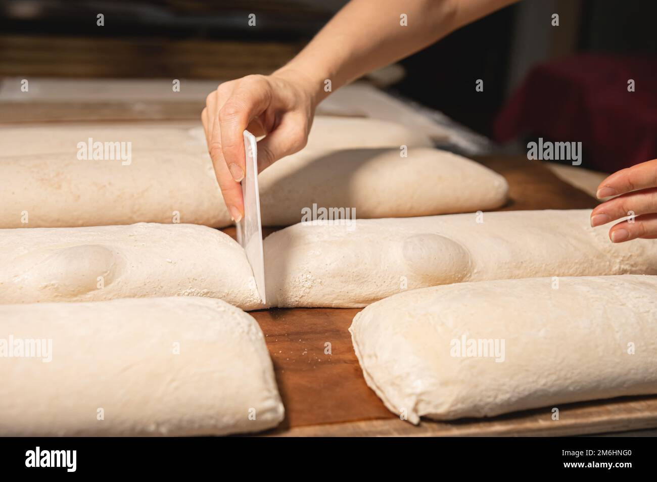 Nahaufnahme der weiblichen Hände einer Bäckerin, die einen Laib Teig mit einer Klinge in einen Laib Brot schneidet, bevor sie im Ofen backen. Craft cr Stockfoto