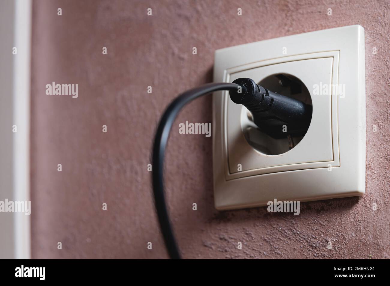 Nahaufnahme eines schwarzen Steckers in einer 220-V-Steckdose in der Wand. Einschaltkonzept Stockfoto