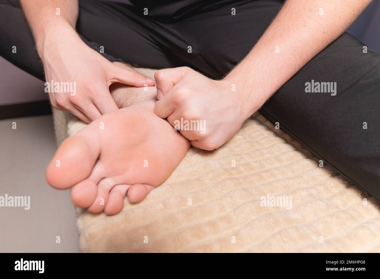 Nahaufnahme eines männlichen Masseurs, der auf einer Koje sitzt, macht sich selbst zu einer heilenden Fußmassage Stockfoto