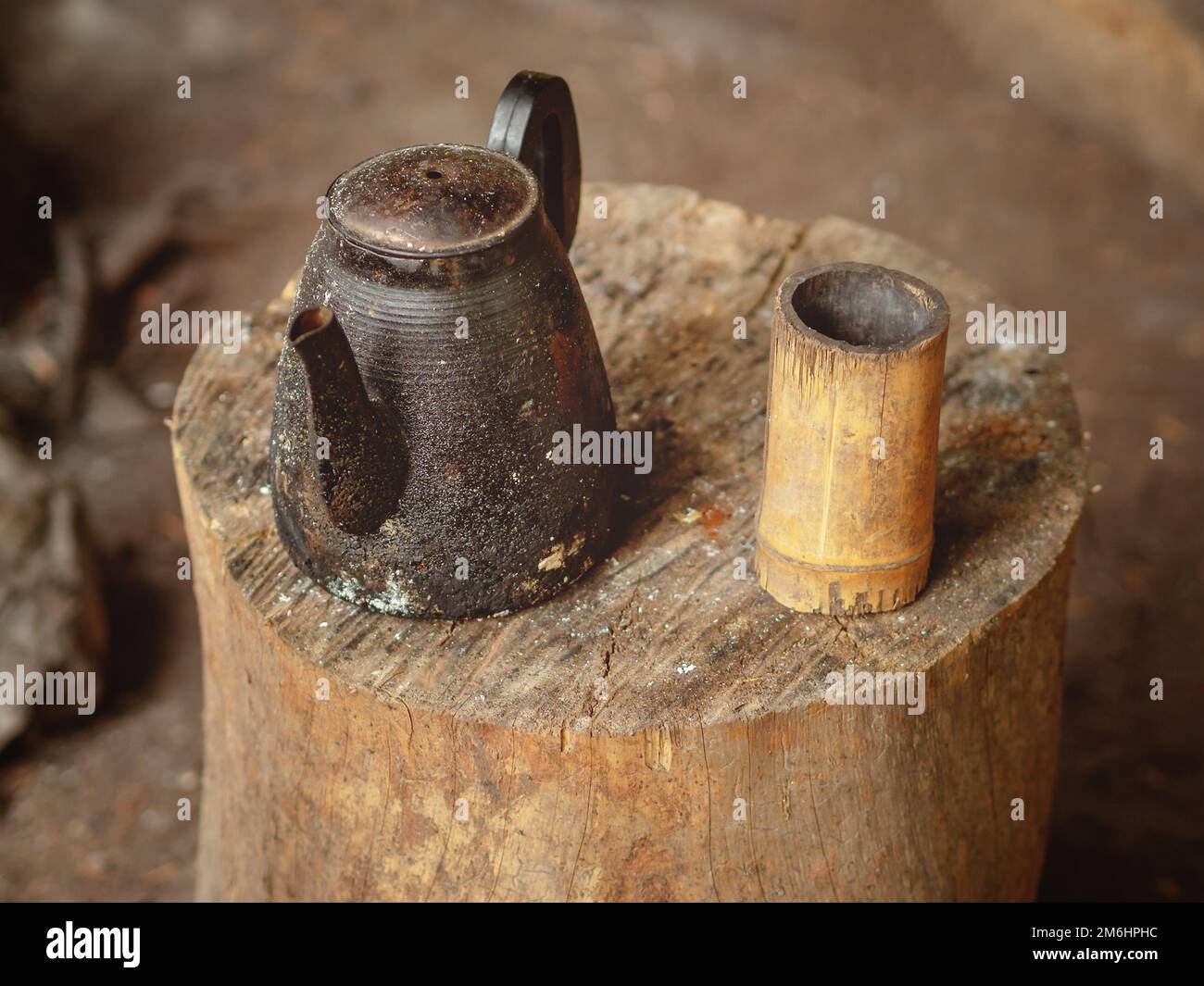 Ein alter verkohlter Wasserkocher mit einer hausgemachten Tasse aus Holz steht auf einem Holzstamm. Teetrinken unter Feldbedingungen Stockfoto
