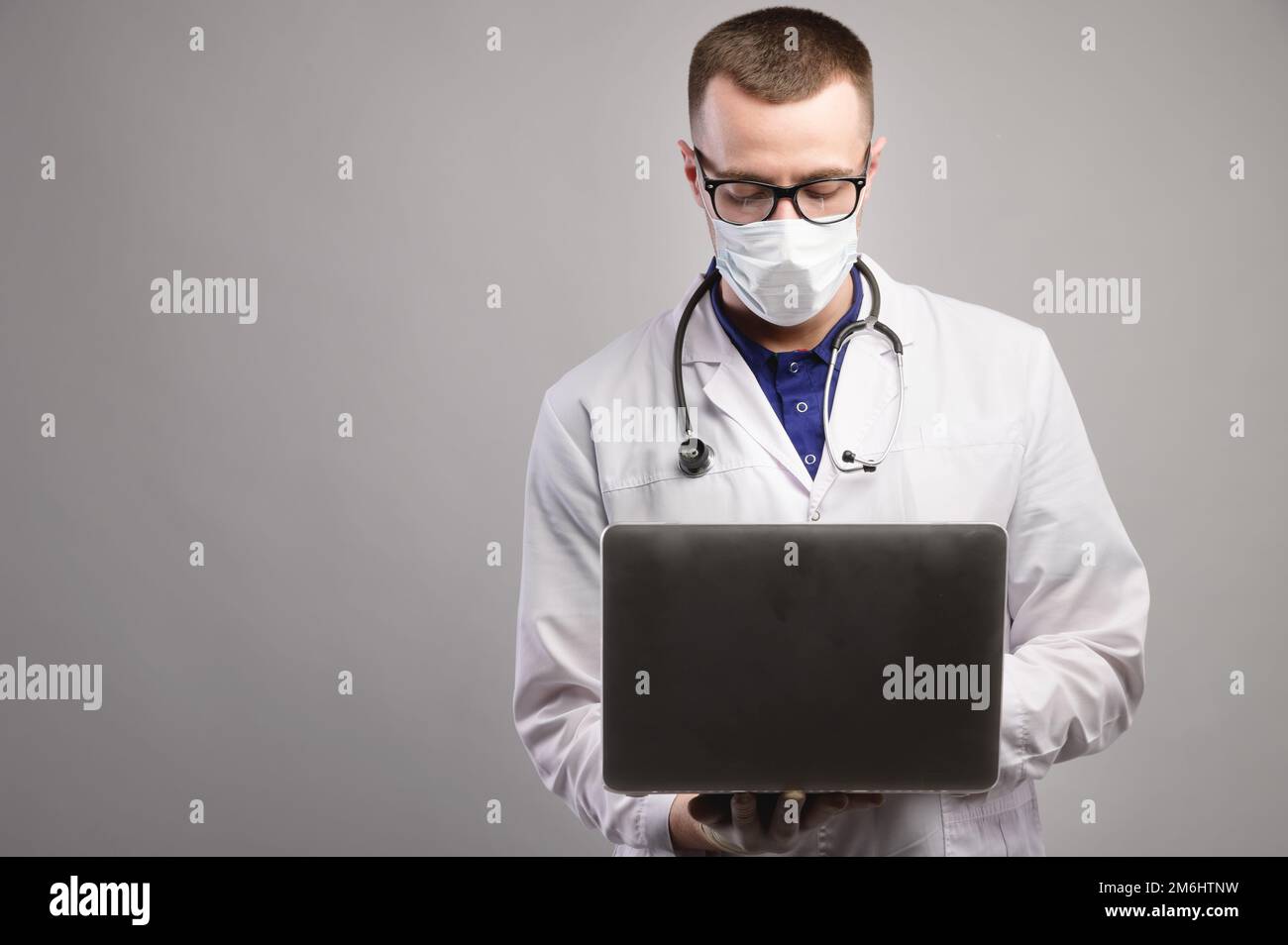 Junger weißer Arzt mit Maske und Brille benutzt seinen Laptop. studioporträt Stockfoto