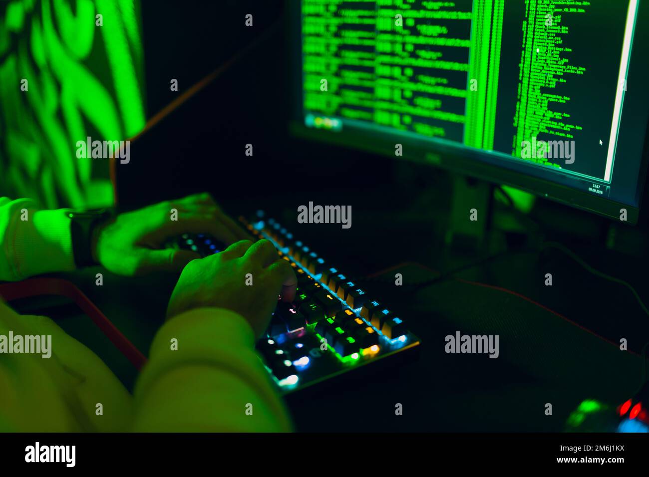 Hacker im Kapuzenpullover hackt Code-Site auf dem PC mit grünem Licht Stockfoto