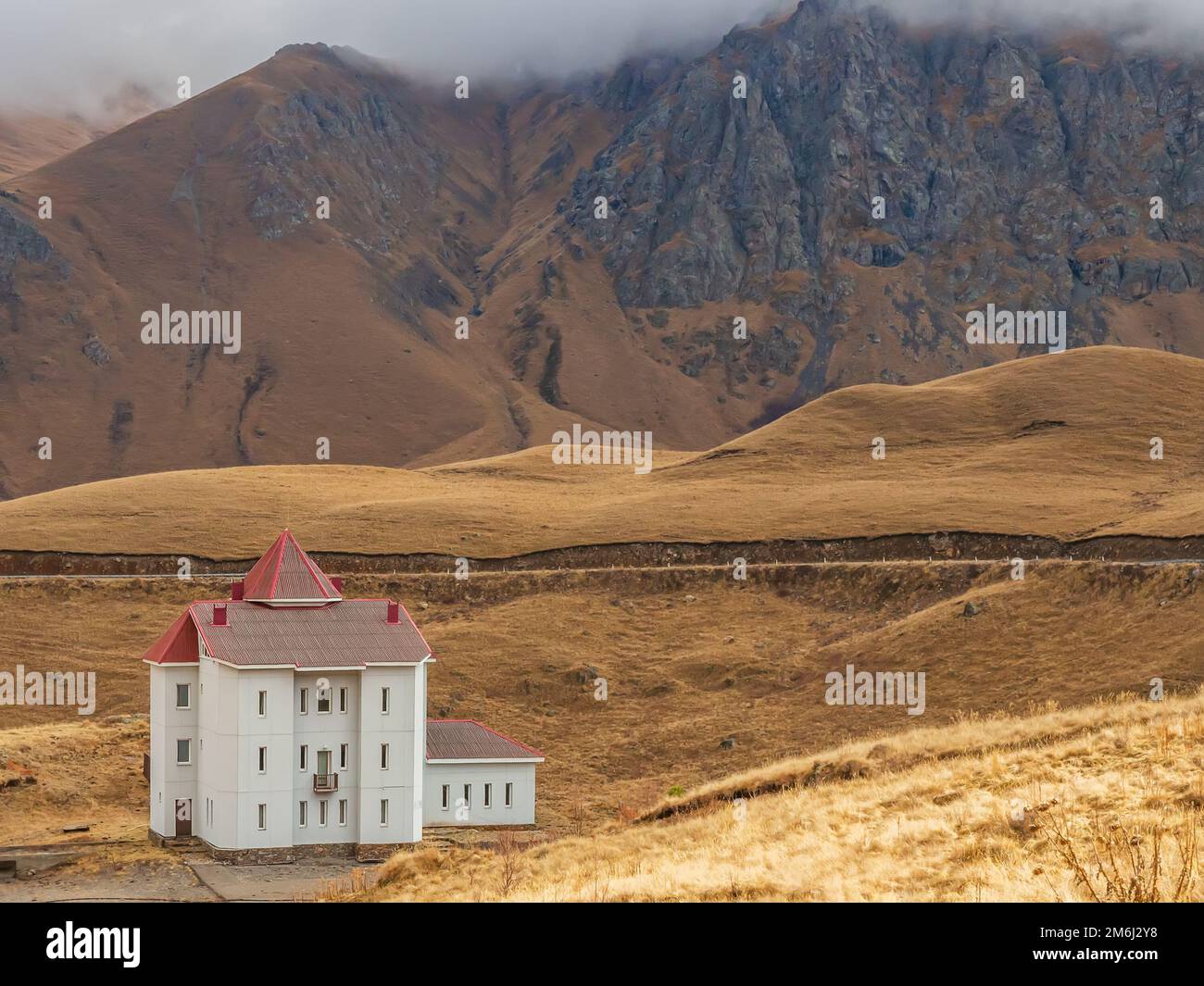 Hoch oben in den Herbstbergen des Kaukasus, wo die Wolken auf den Gipfeln liegen, gibt es ein weißes Haus mit schmalen Fenstern und Stockfoto