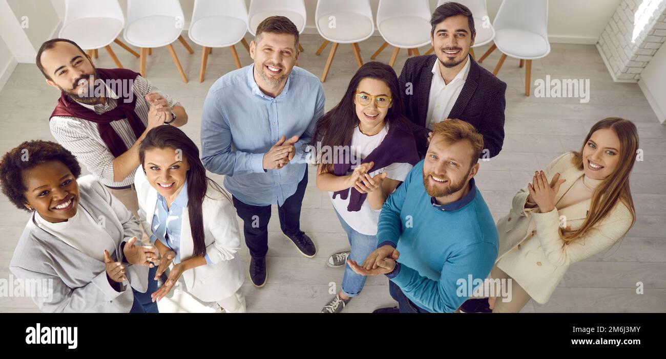 Multiethnisches Team aus glücklichen jungen Geschäftsleuten, die im Amt stehen, lächeln und applaudieren Stockfoto