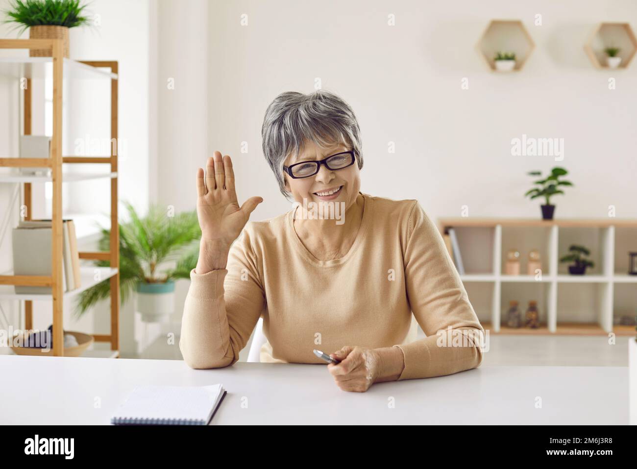 Glückliche Seniorin, die während eines Videoanrufs oder einer Onlinekonferenz lächelt und ihnen winkt Stockfoto