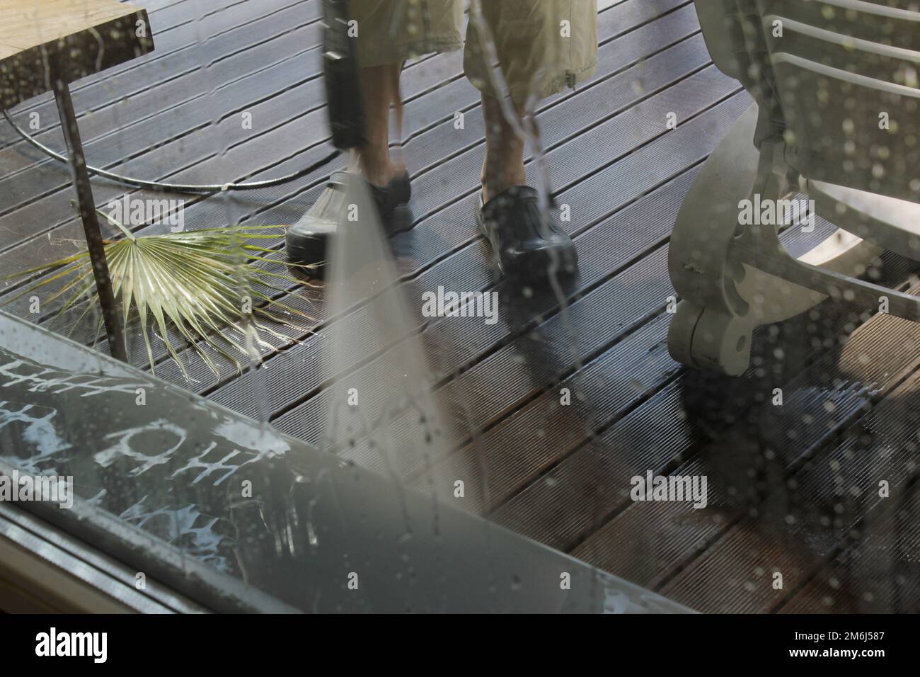 Leistungsstarke Oberflächenreinigung. Ein Mann, der die Terrasse mit einem Hochdruckreiniger reinigt. Hochdruckreiniger auf Holzterrasse und Gartenmöbeln. Stockfoto