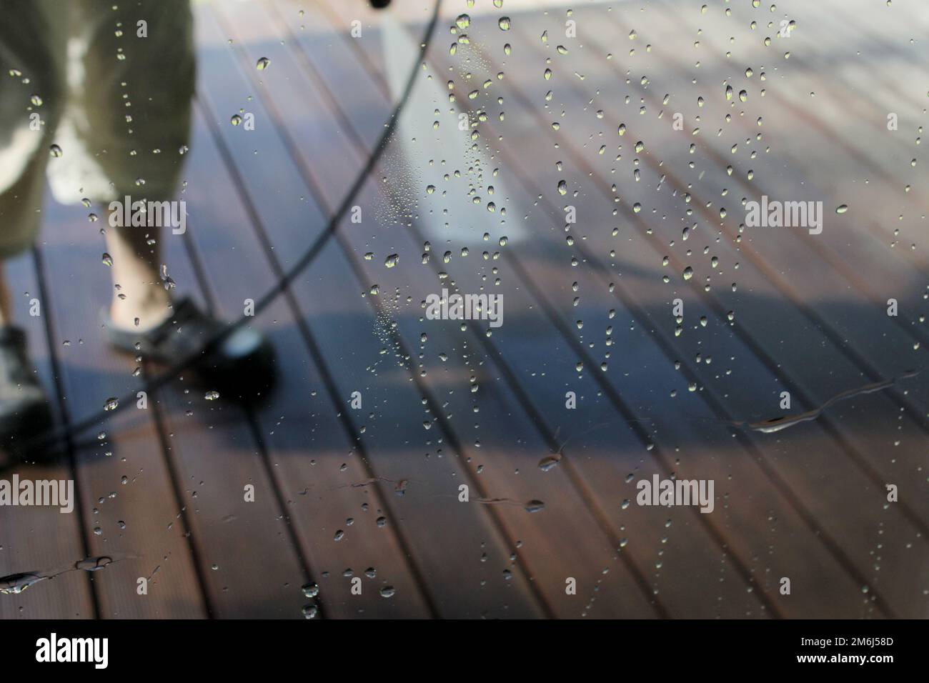 Leistungsstarke Oberflächenreinigung. Ein Mann, der die Terrasse mit einem Hochdruckreiniger reinigt. Hochdruckreiniger auf Holzterrasse. Stockfoto