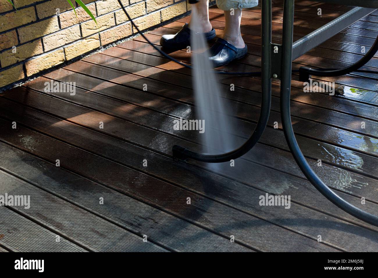 Leistungsstarke Oberflächenreinigung. Ein Mann, der die Terrasse mit einem Hochdruckreiniger reinigt. Hochdruckreiniger auf Holzterrasse und Gartenmöbeln. Stockfoto