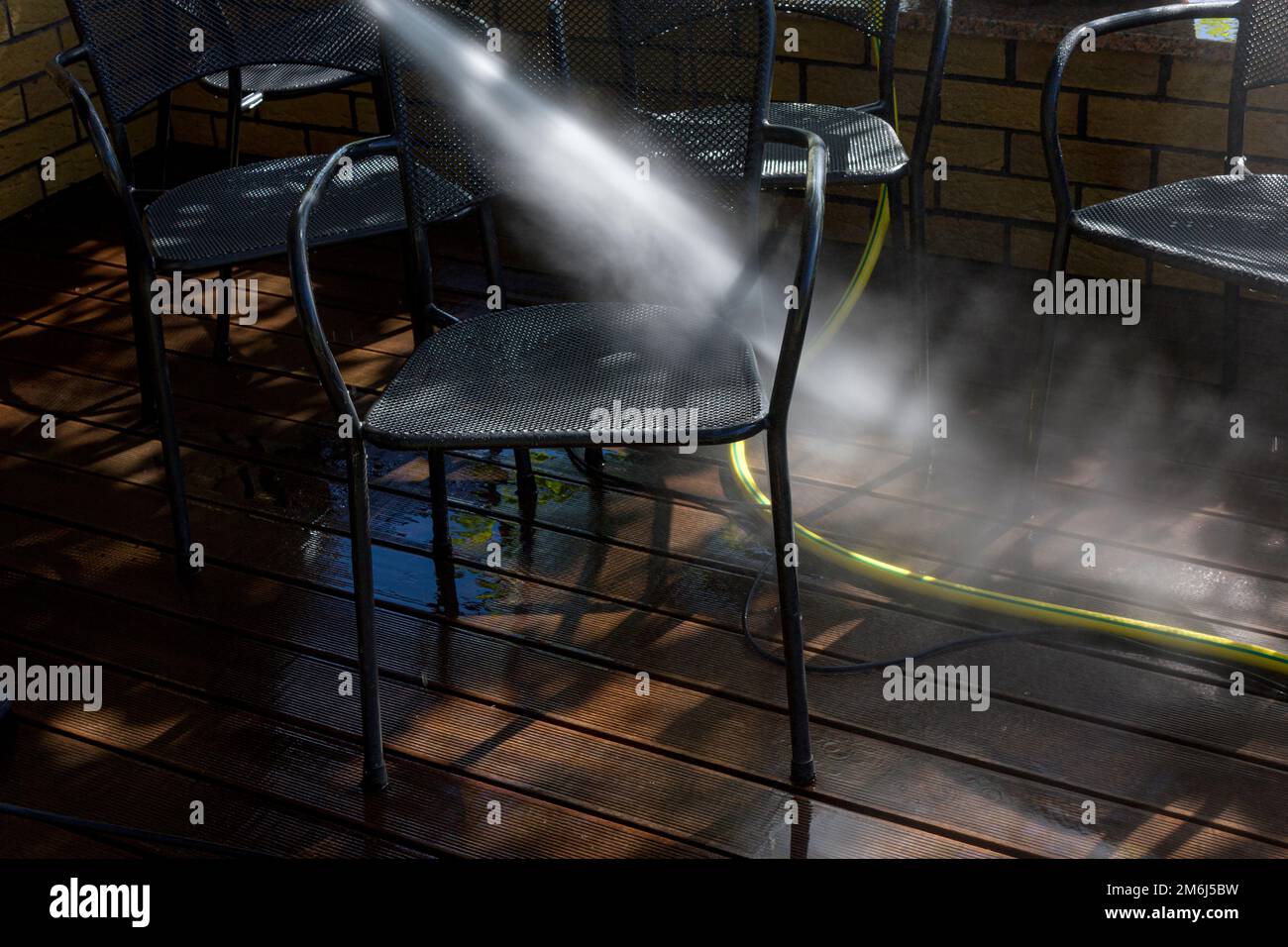 Leistungsstarke Oberflächenreinigung. Ein Mann, der die Terrasse mit einem Hochdruckreiniger reinigt. Hochdruckreiniger auf Holzterrasse und Gartenmöbeln. Stockfoto