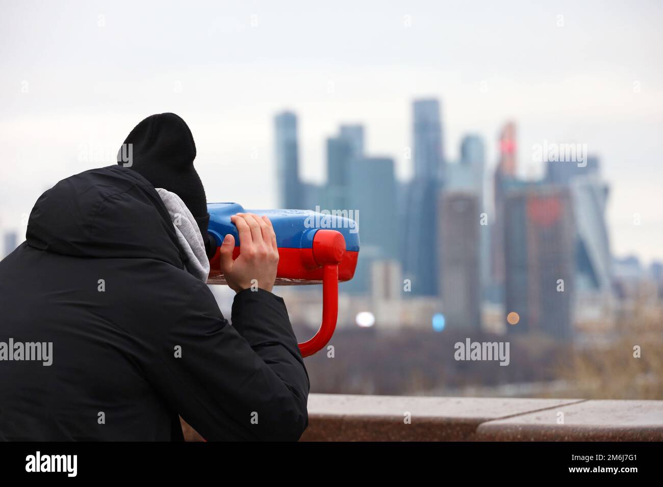 Mann, der ein Fernglas benutzt, um das Panorama der Stadt Moskau zu betrachten. Touristen auf der Aussichtsplattform im Winter Stockfoto