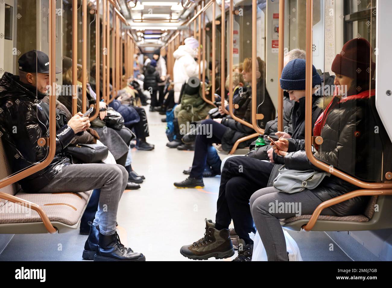 Moskau, Russland - Januar 2023: Menschen in einem U-Bahn-Zug im Winter, Passagiere sitzen mit Smartphones. Das Innere eines modernen U-Bahn-Wagens Stockfoto