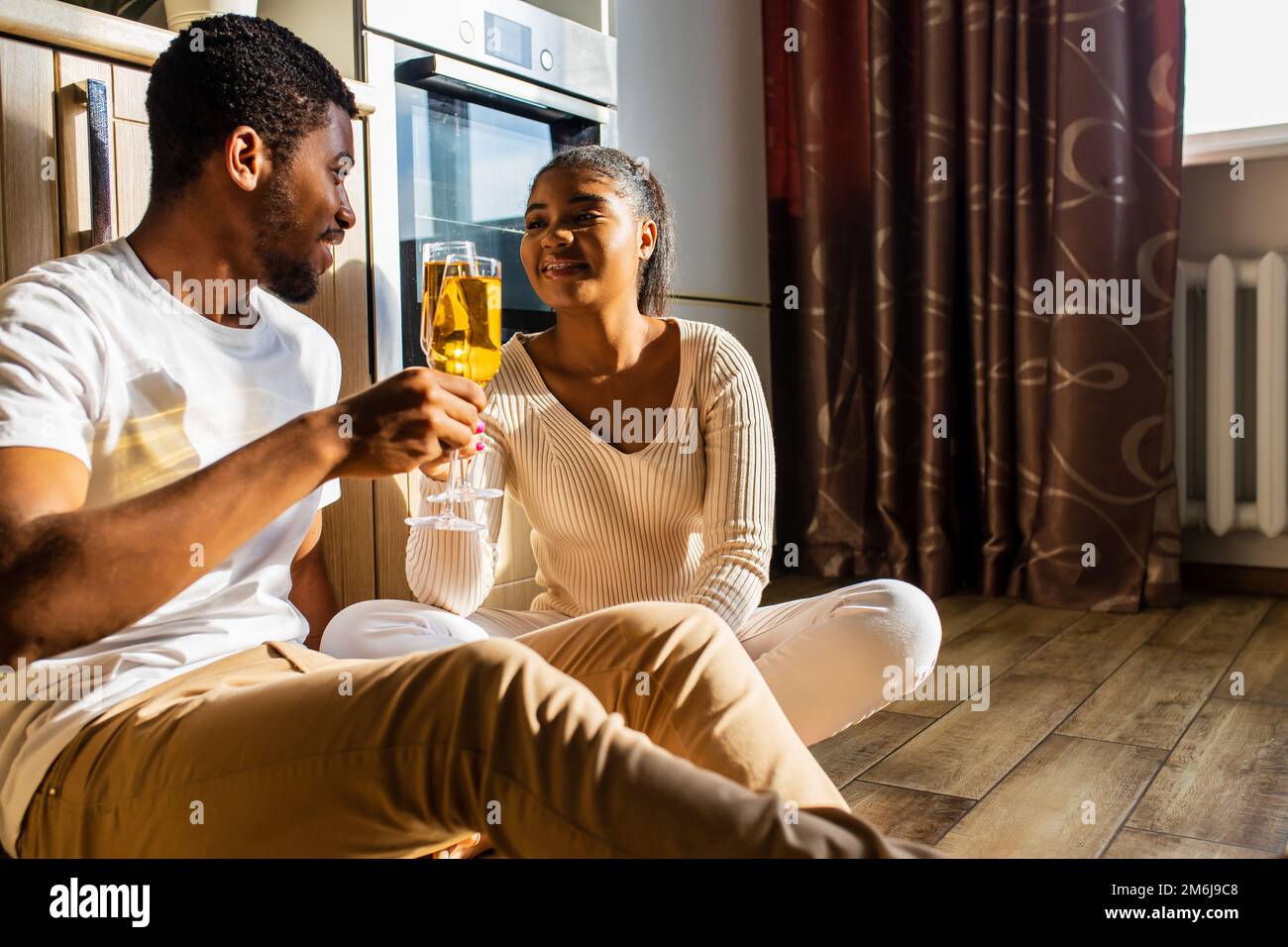 Glückliches Paar, das seinen Hochzeitstag feiert, während es auf dem warmen Boden in der Küche sitzt Stockfoto