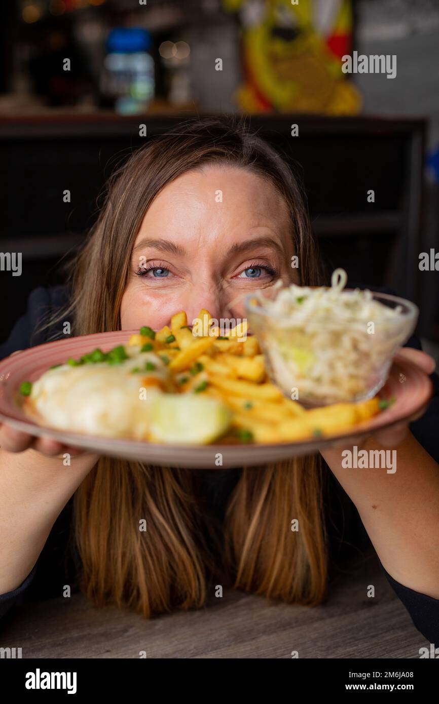 Fröhliche Frau, die sich in den Händen hält, mit Pommes Frites, Hühnerfilet und Gemüsesalat. Servieren von Hauptgericht und Garnierung Nahaufnahme, selektiver Fokus Stockfoto