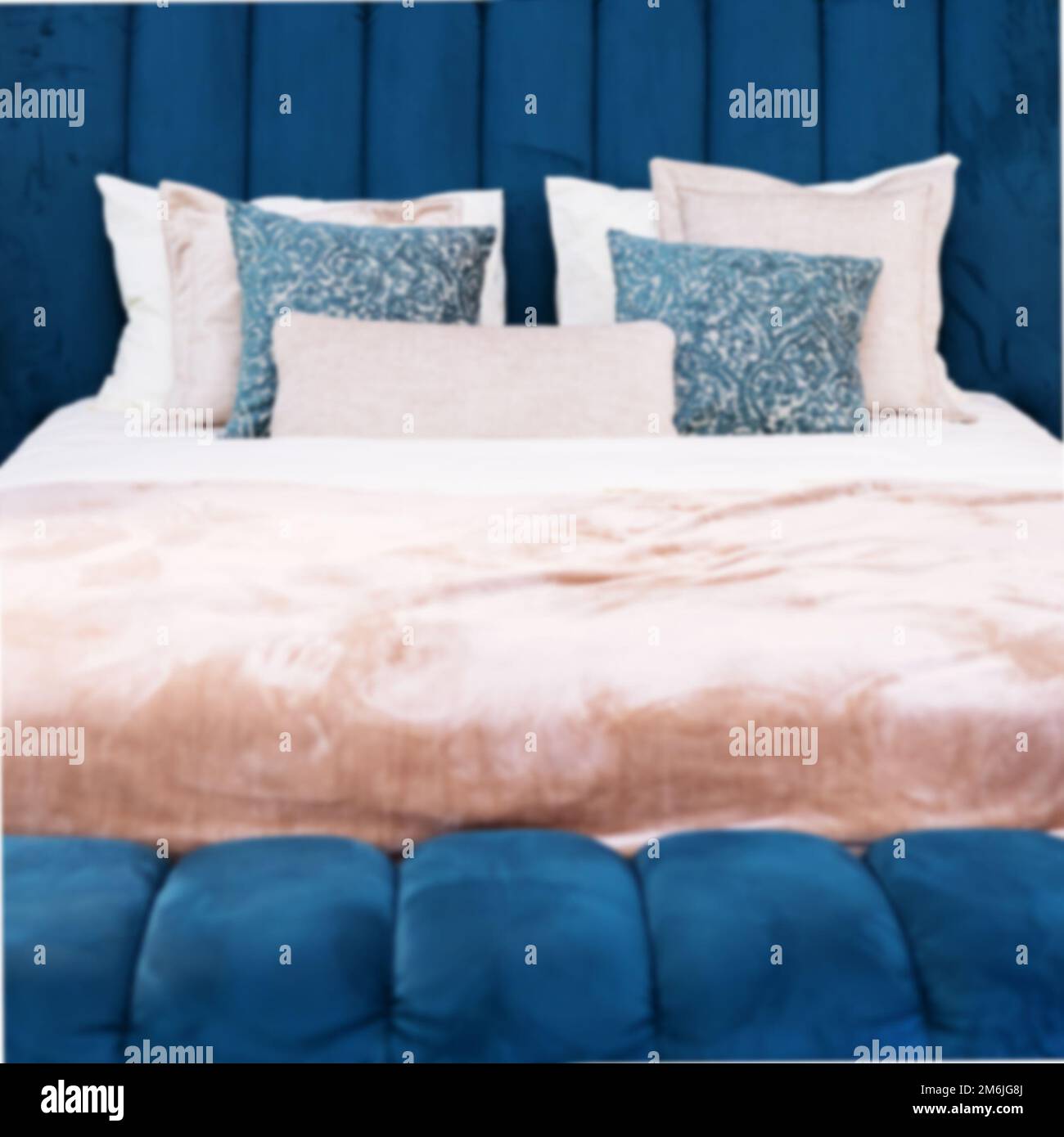 Ein weiches blaues Samtbett mit pinkfarbenem Bettüberwurf und Kissen in verschiedenen Größen. Unschärfe-Effekt im Vollbildmodus Stockfoto