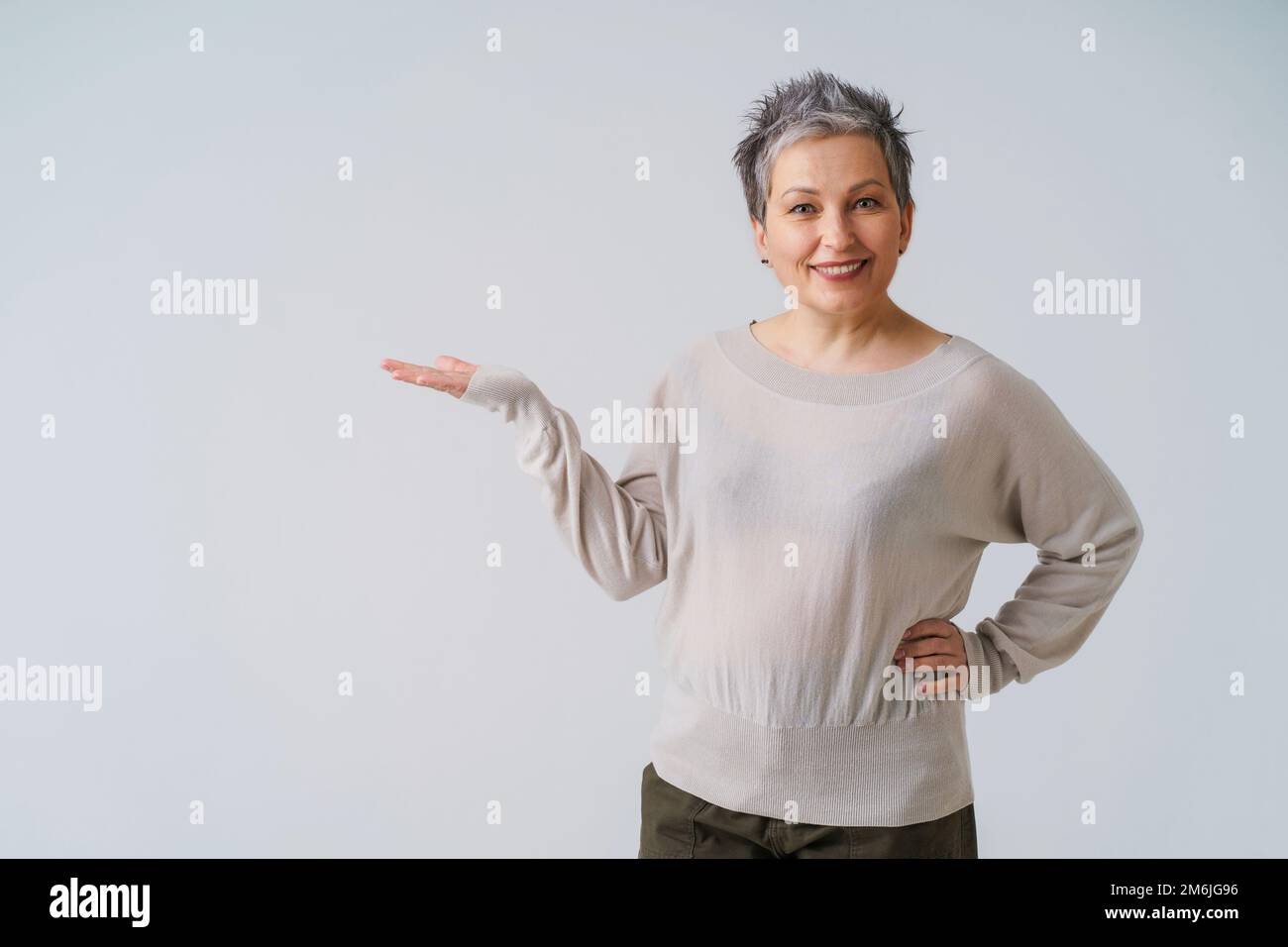 Wunderschöne, wunderschöne 50s-jährige Frau mit grauen Haaren, die mit der Hand nach oben für die Produktplatzierung posiert, isoliert auf weißem Hintergrund. Stockfoto