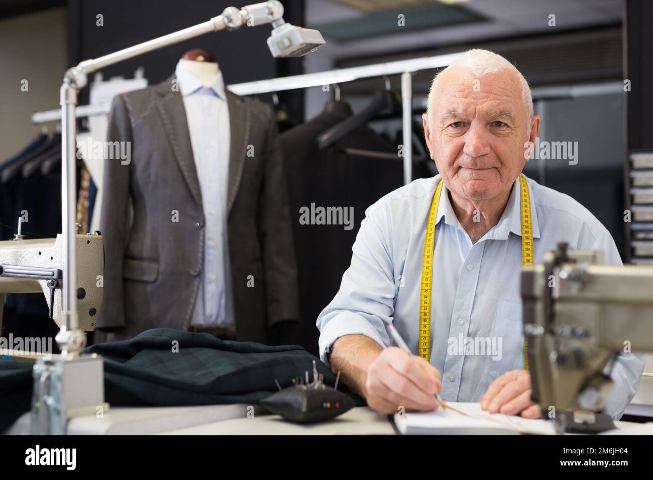 Der ältere Schneidermann nimmt Messungen aus seiner Jacke und schreibt sie in der Werkstatt in ein Notizbuch Stockfoto
