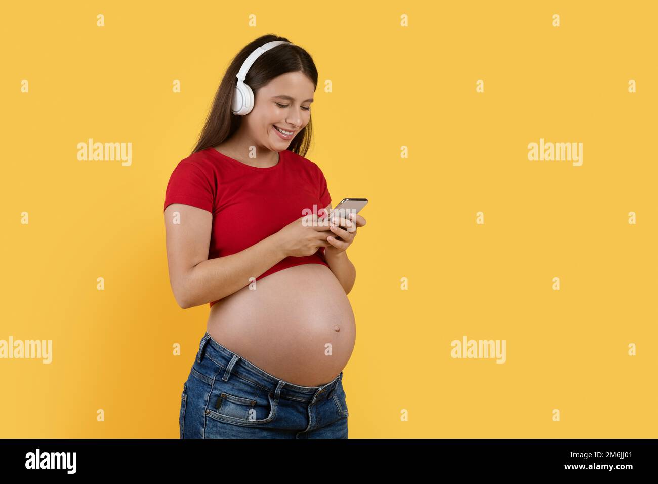 Moderne Technologien. Glückliche Schwangere Mit Kabellosen Kopfhörern, Die Musik Auf Dem Smartphone Hört Stockfoto