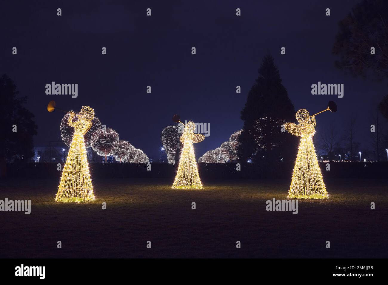 Drei Weihnachtsengel aus leuchtenden Girlanden beleuchten den Park mit seinen runden, leuchtenden Bäumen im n Stockfoto
