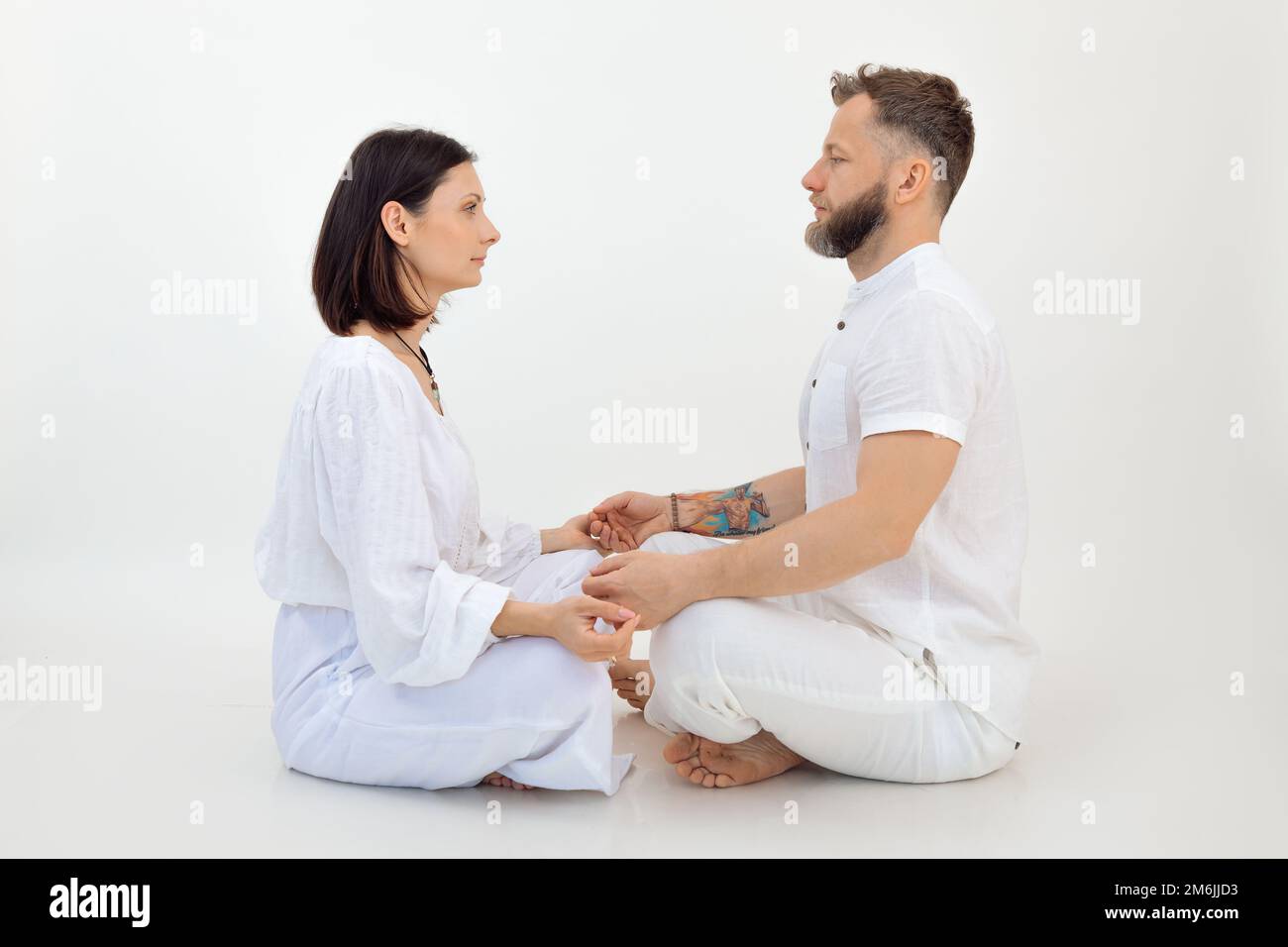 Ruhige, sportliche Familie von Frauen, Mann sitzt mit gekreuzten Beinen, schaut sich an, hält Hände auf weißem Hintergrund. Stockfoto