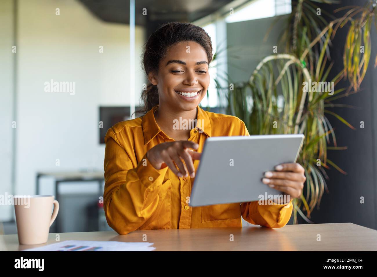 Moderne Technologien in der Wirtschaft. Glückliche schwarze Geschäftsfrau, die ein modernes digitales Tablet verwendet und online im Büro arbeitet Stockfoto