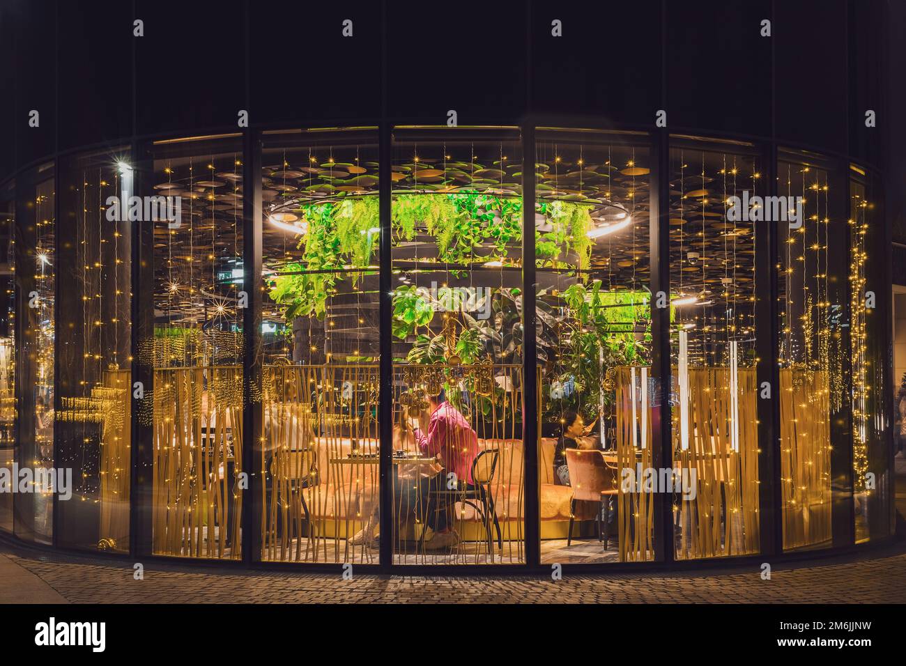 Russland, Krasnodar 07.01.2022. Abendcafé mit grünen Pflanzen und Girlanden an Panoramafenstern. Romantische Nacht Stockfoto