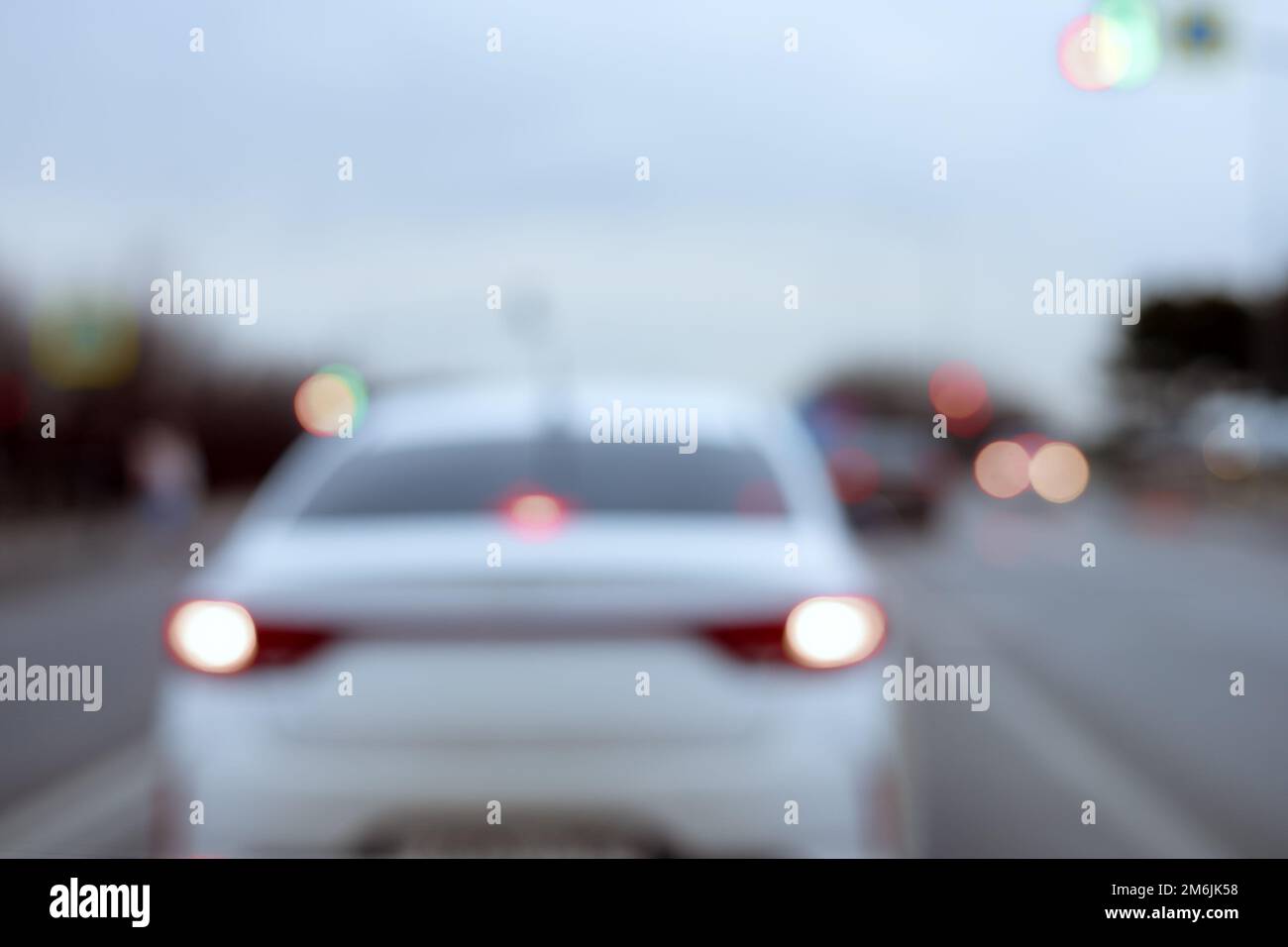 Ein weißes Auto mit eingeschalteten Scheinwerfern fährt bei bewölktem Wetter die Straße entlang. Unschärfe-Effekt. Stockfoto