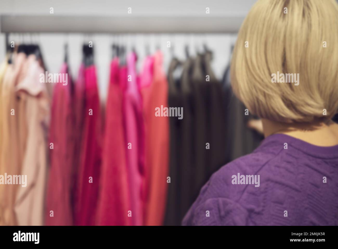 Die Blonde wählt eine Jacke, die an einem Kleiderbügel hängt. Verkauf in einem Modegeschäft. Unschärfe-Effekt Stockfoto