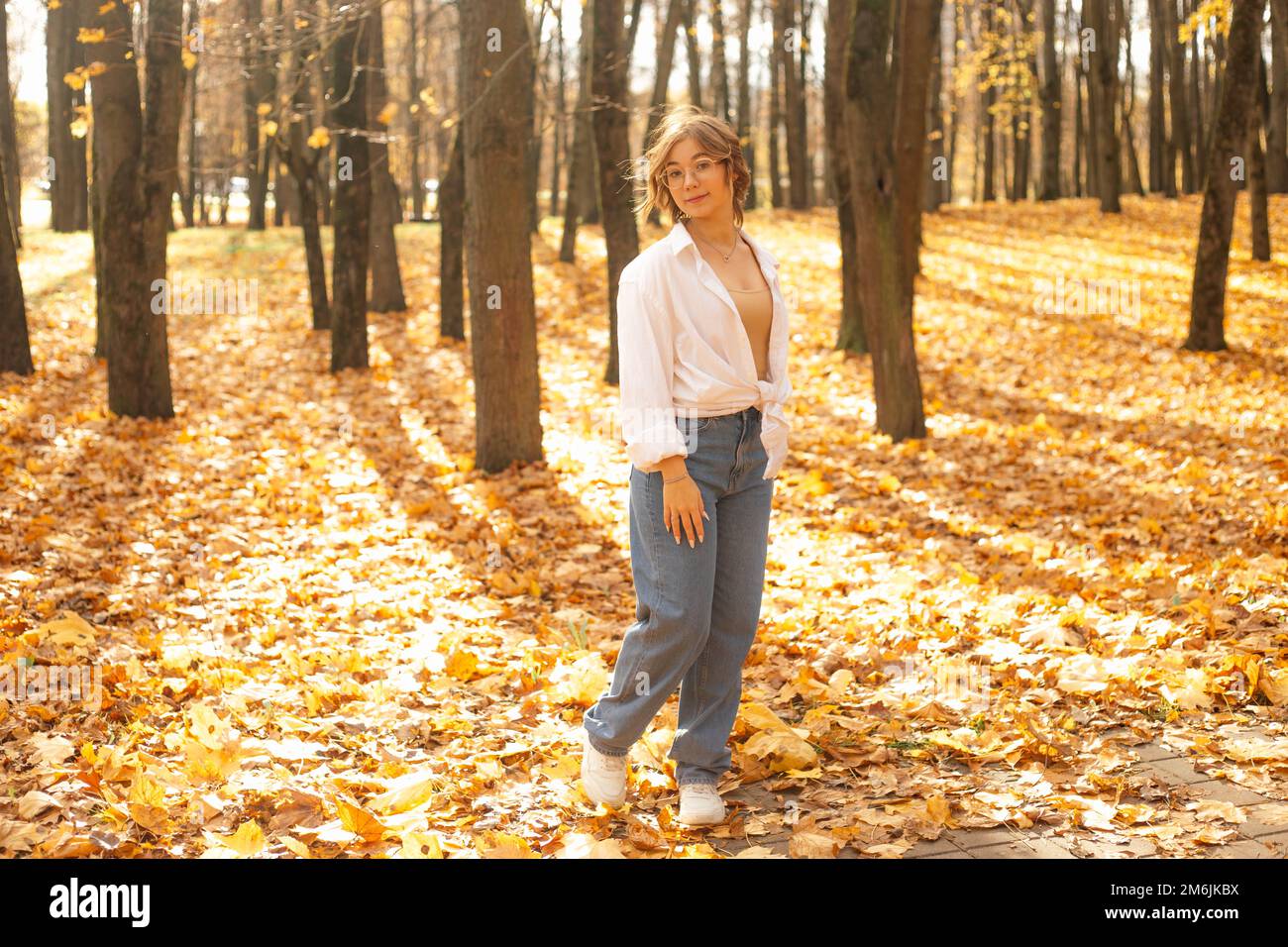 Porträt eines jungen, fantastischen Teenagers, das an einem sonnigen Herbsttag im Park zwischen Bäumen auf gelben Ahornblättern steht. Stockfoto