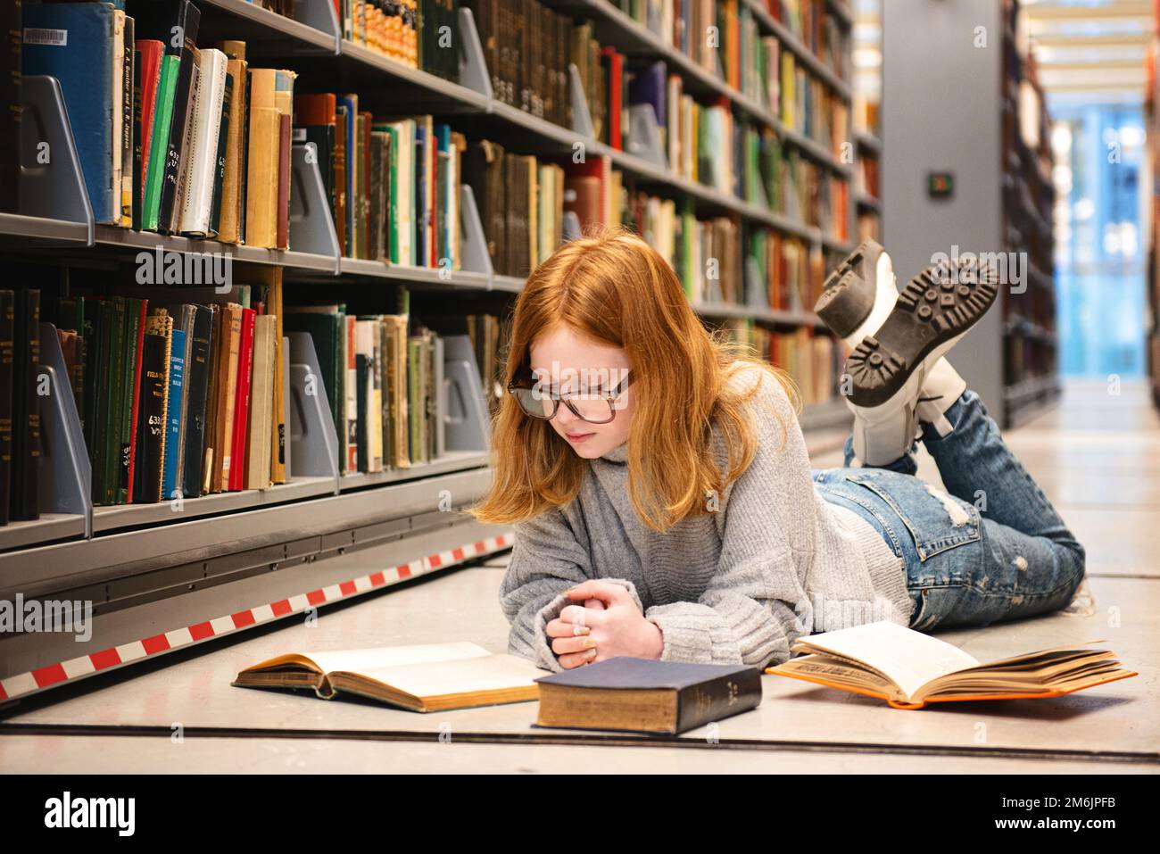 Teenager mit roten Haaren lag auf dem Bibliotheksboden und las. Stockfoto