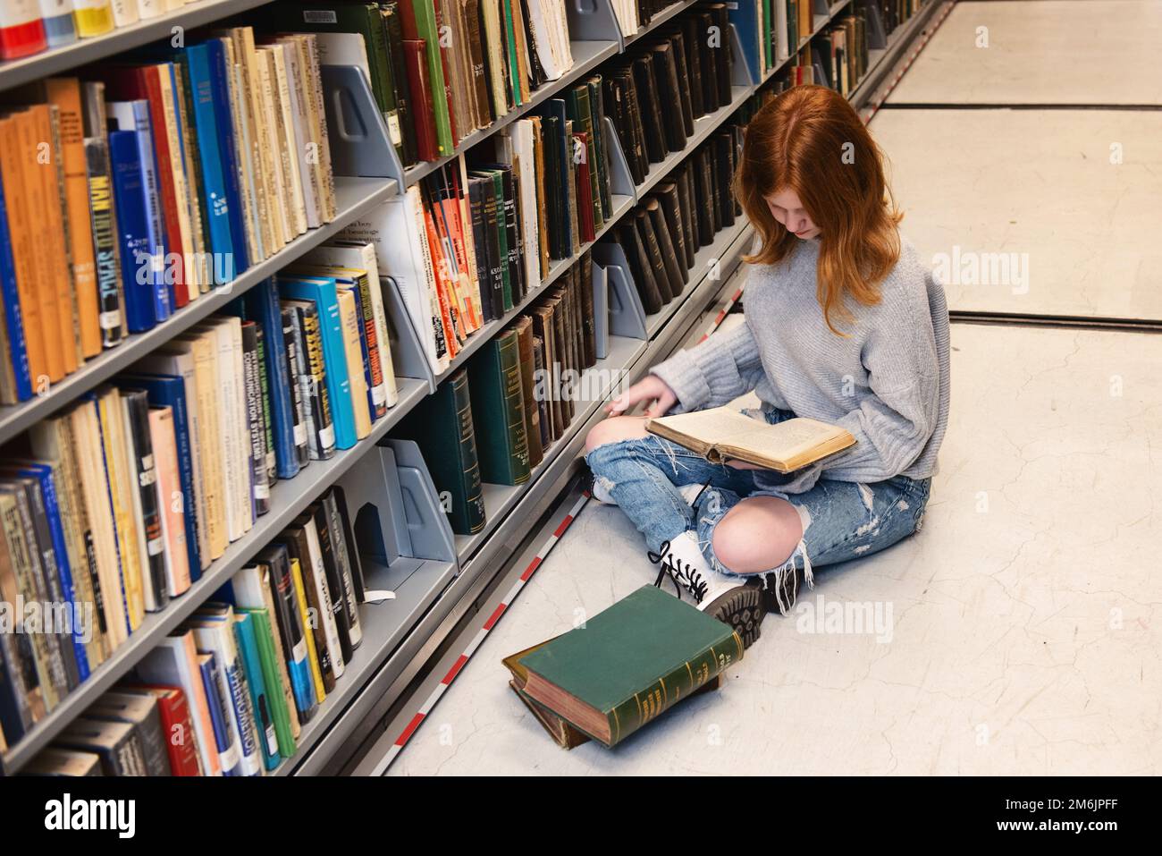 Teenager Redhead Girl sitzt mit einem Stapel Bücher in der Bibliothek Stockfoto