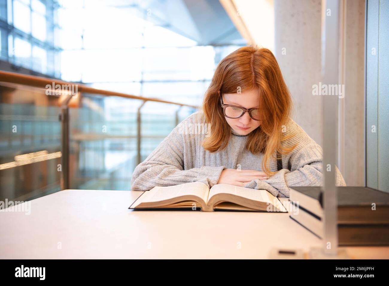 Teenager mit roten Haaren und Brille, die in einer städtischen Bibliothek studiert. Stockfoto