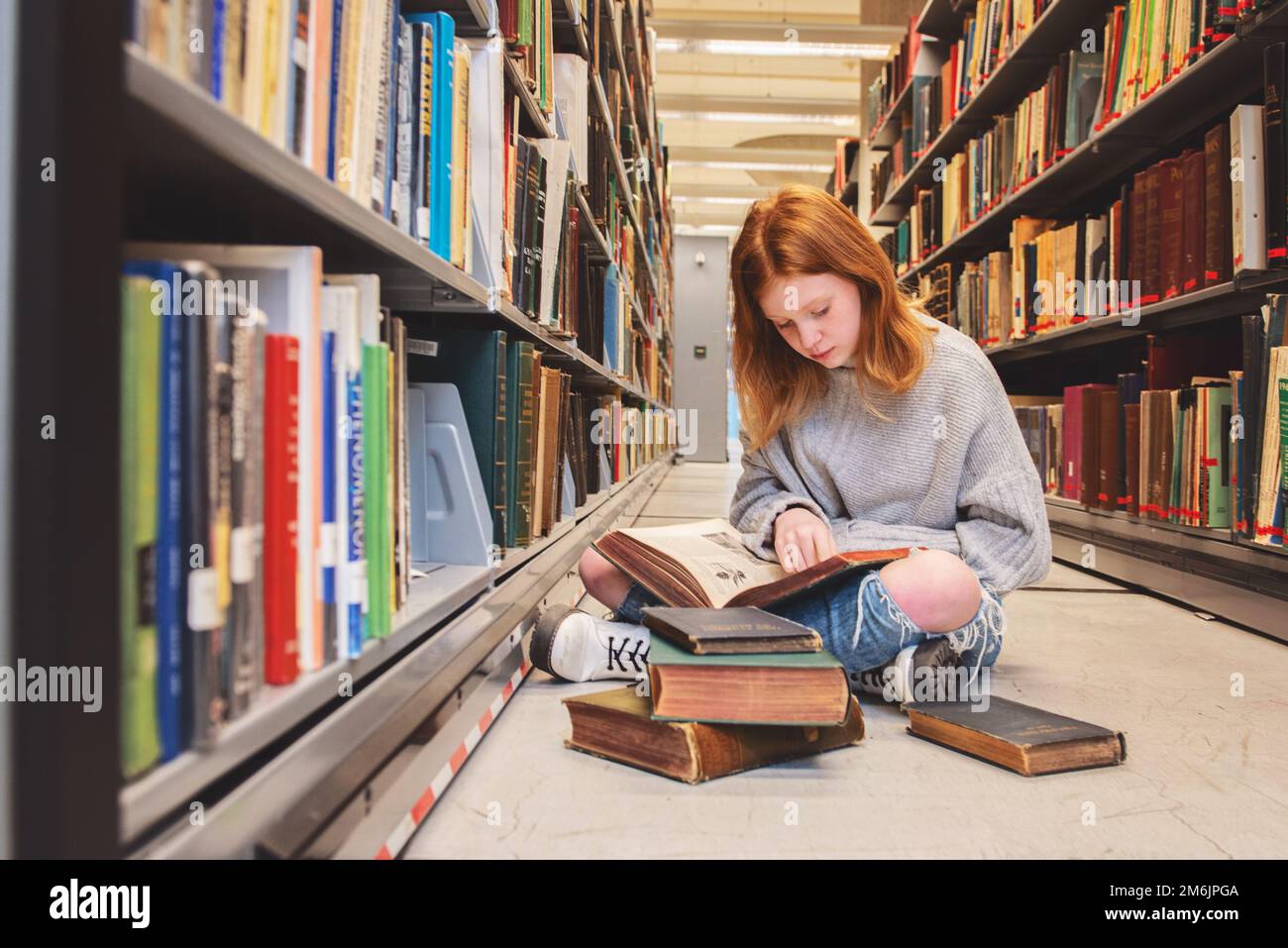 Teenager Redhead Girl sitzt mit einem Stapel Bücher in der Bibliothek Stockfoto