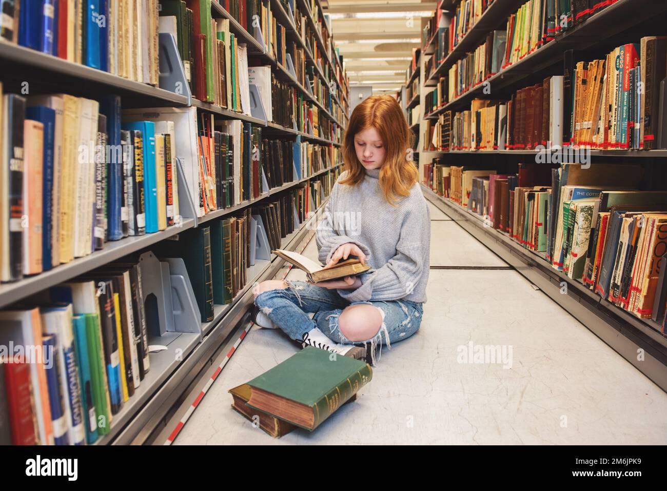 Teenager, die mit einem Buch in der Bibliothek sitzt. Stockfoto
