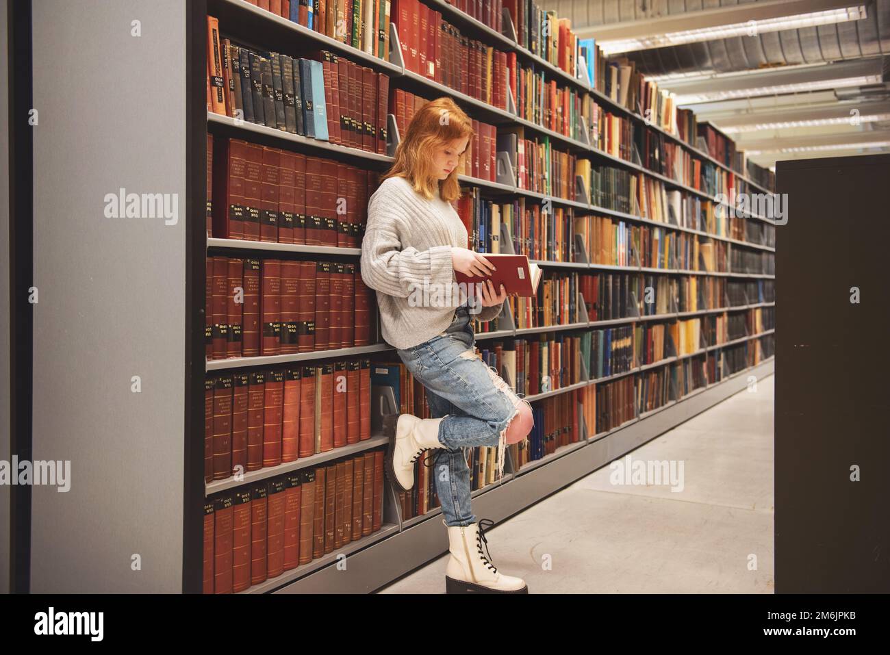 Teenager mit roten Haaren stehen neben Regalen Bibliotheksleser. Stockfoto