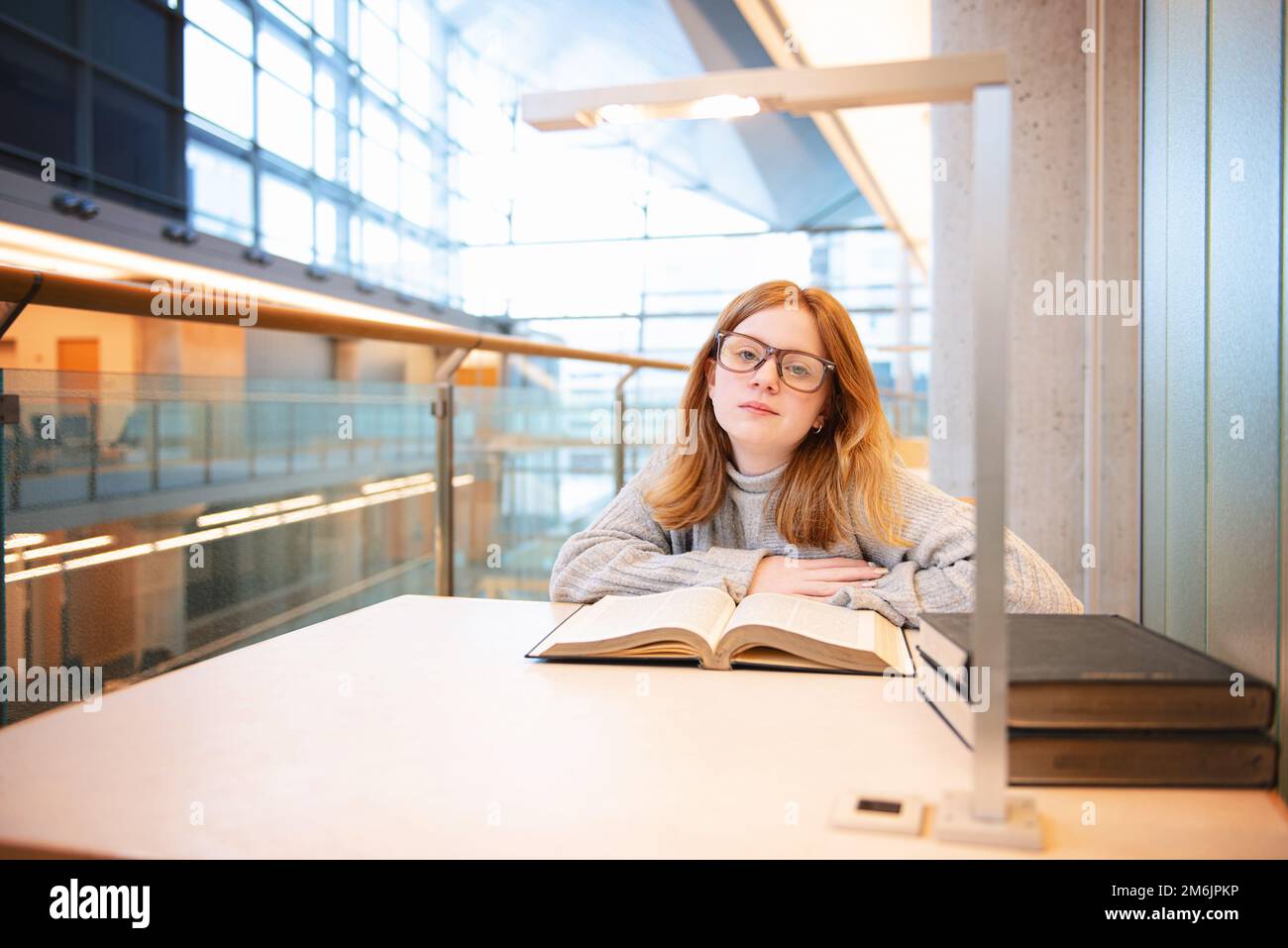 Teenager mit roten Haaren und Brille liest in der Bibliothek. Stockfoto