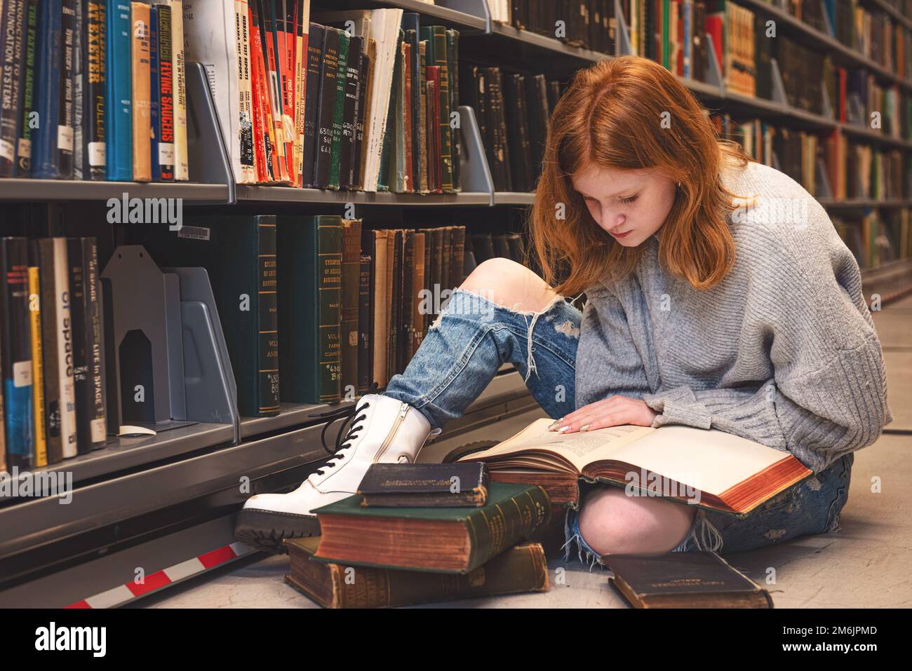 Teenager, die auf dem Boden sitzt und in der Bibliothek liest. Stockfoto