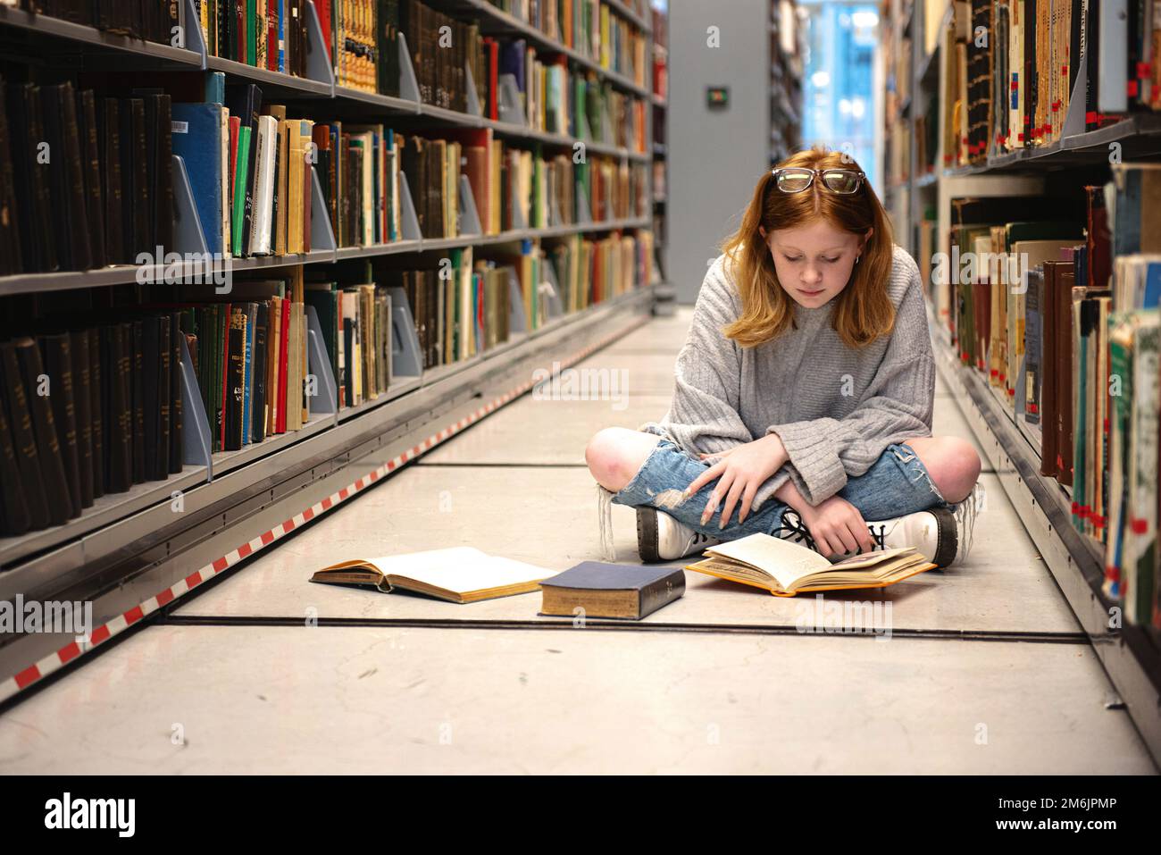 Teenager mit roten Haaren und Brille, die in der Bibliothek lernt. Stockfoto