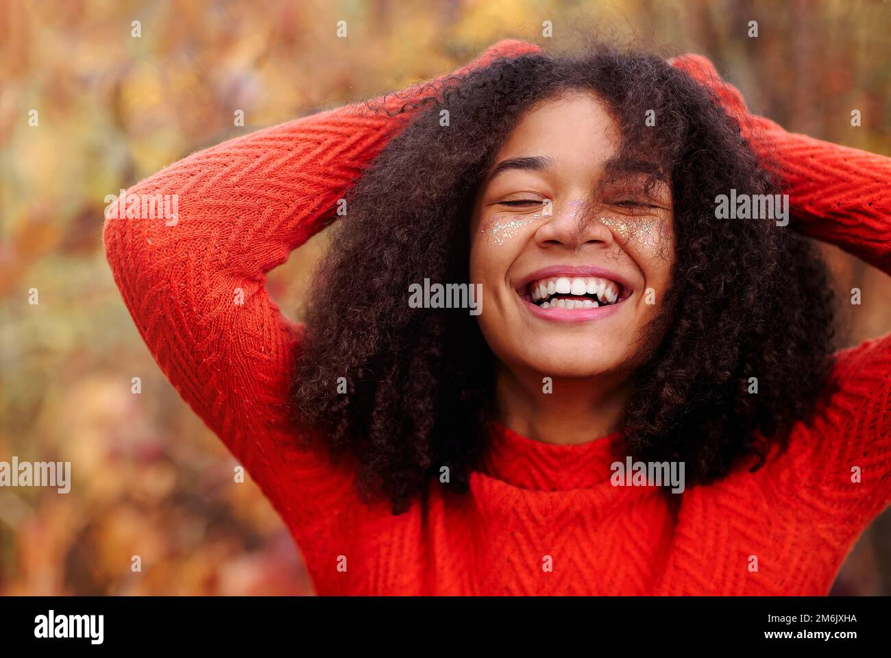 Junge, glückliche, lockige afroamerikanische Frau mit geschlossenen Augen und lachend im Herbstwald Stockfoto