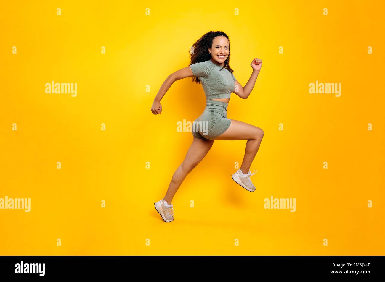 Sportlicher Lifestyle. Foto in voller Länge einer sportlichen, fröhlichen brasilianerin oder Latino-Frau in Sportbekleidung, Training, Springen, Laufen, Lächeln vor der Kamera, Isolierter orangefarbener Hintergrund Stockfoto