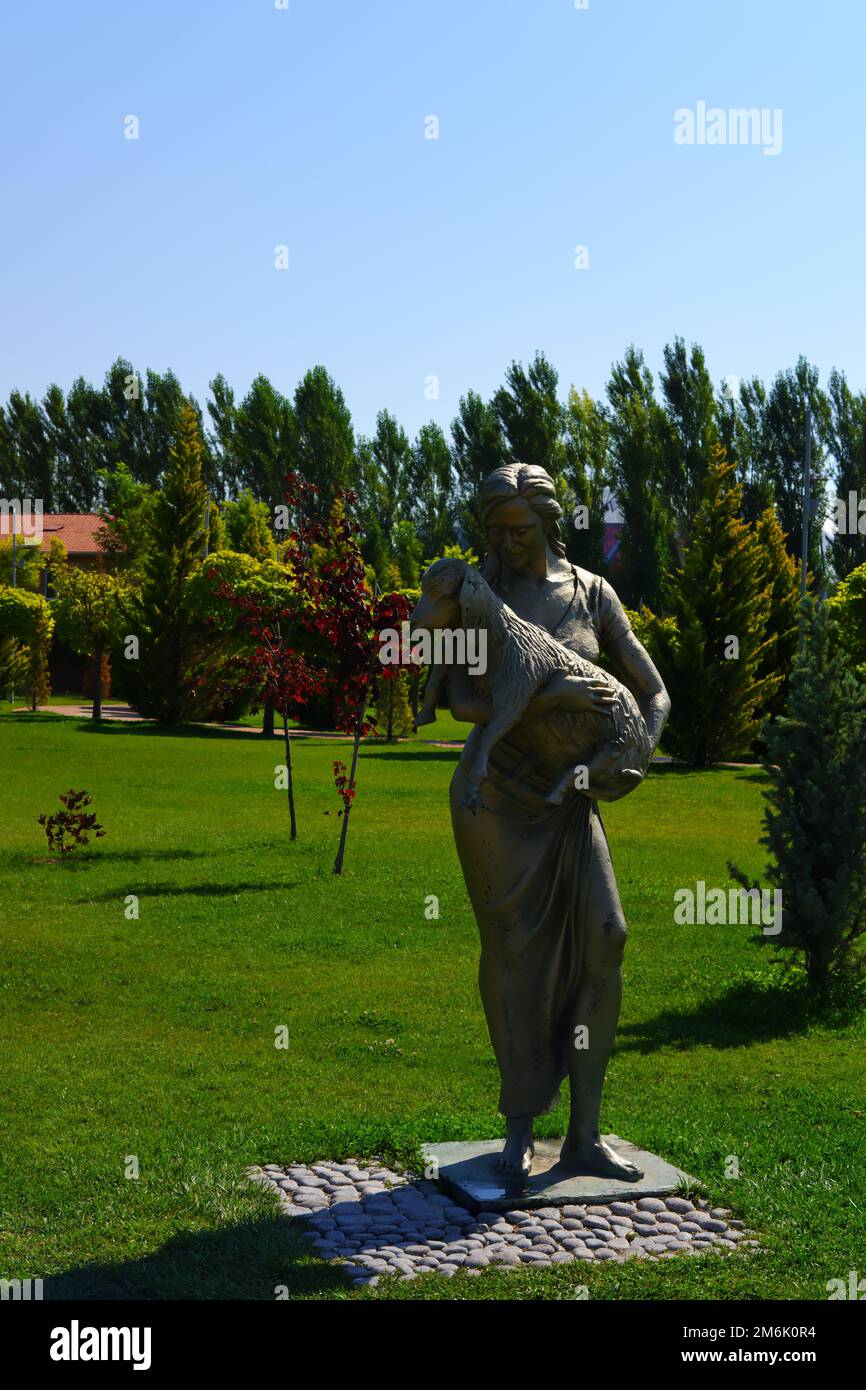 Statue einer Frau, die an einem sonnigen Tag im Park in Bäumen Lamm an den Händen hält Stockfoto