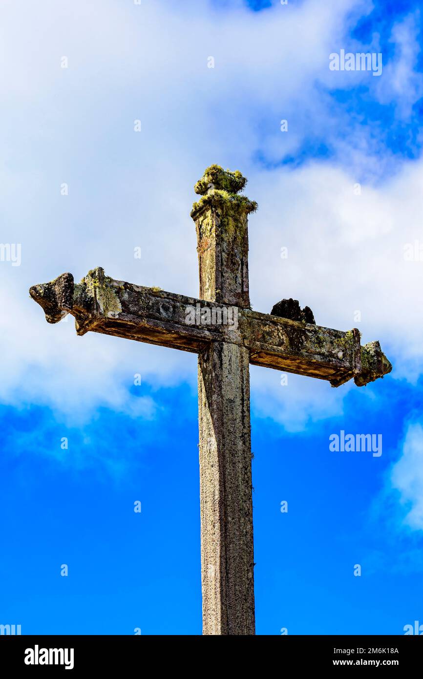 Katholisches Kruzifix aus altem Stein, bedeckt mit parasitären Pflanzen und Moos Stockfoto