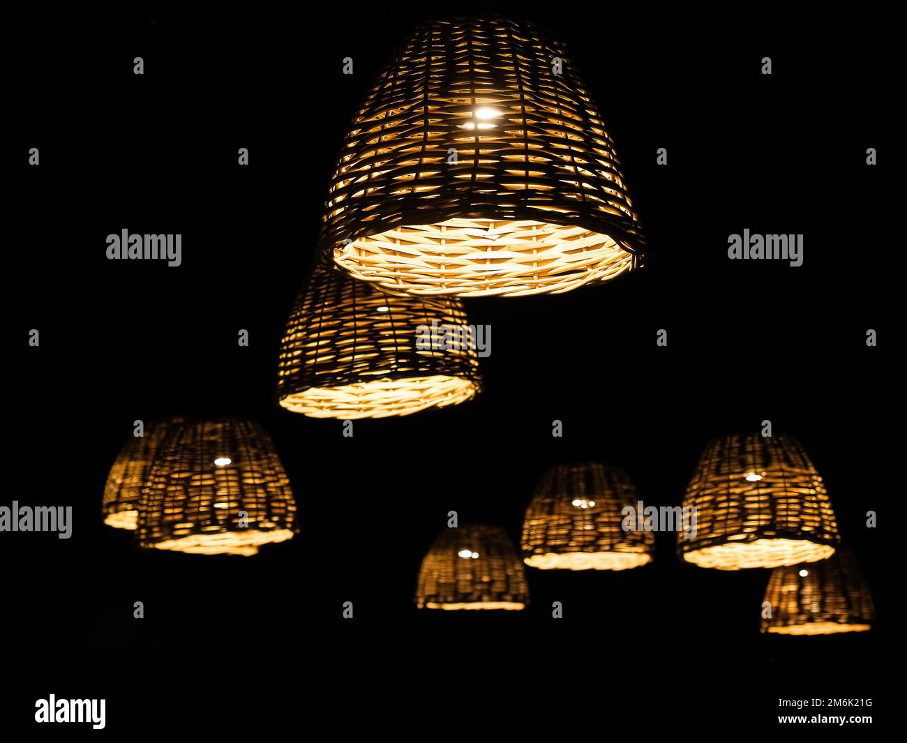 Viele Lampen mit Rattlampenschirmen hängen im Dunkeln. Nachtparkbeleuchtung. Selektiver Fokus. Stockfoto